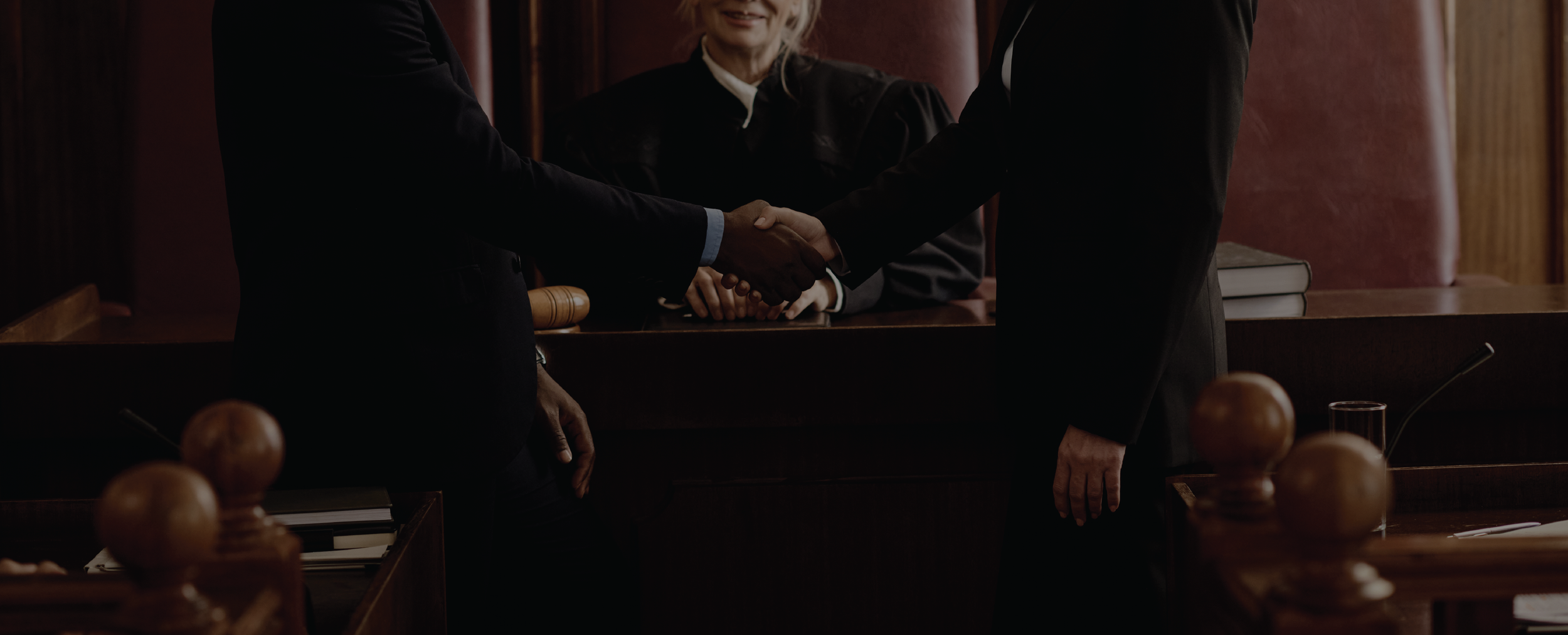 Dos personas en trajes de negocios se dan la mano en un entorno de sala de audiencias y una jueza observa desde atrás.