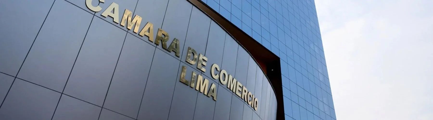 Edificio moderno con fachada de cristales azules y letras doradas que dicen 'Cámara de Comercio Lima'.