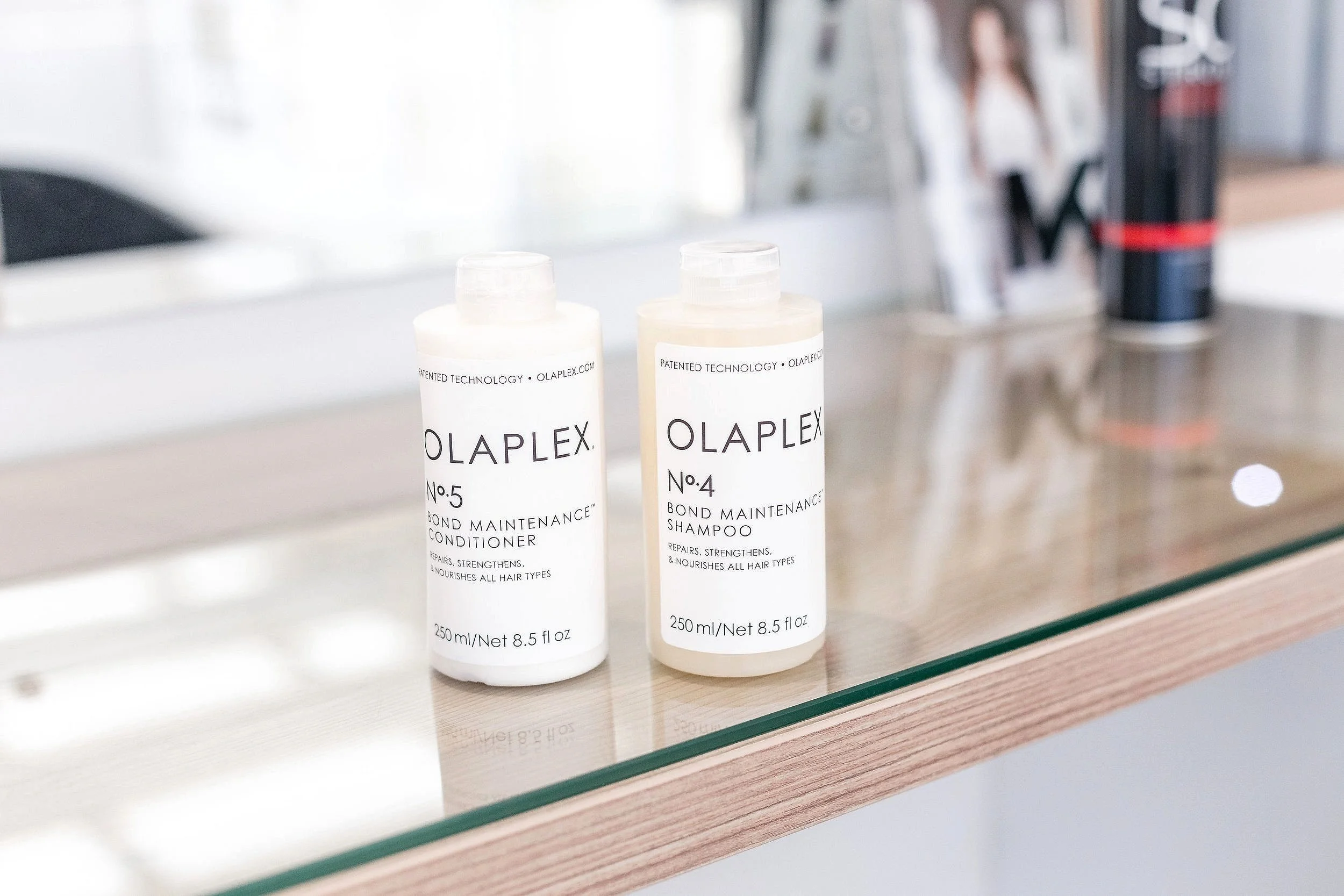 Two bottles of Olaplex hair care products, Bond Maintenance Conditioner and Shampoo, sitting on a wooden surface in a salon.