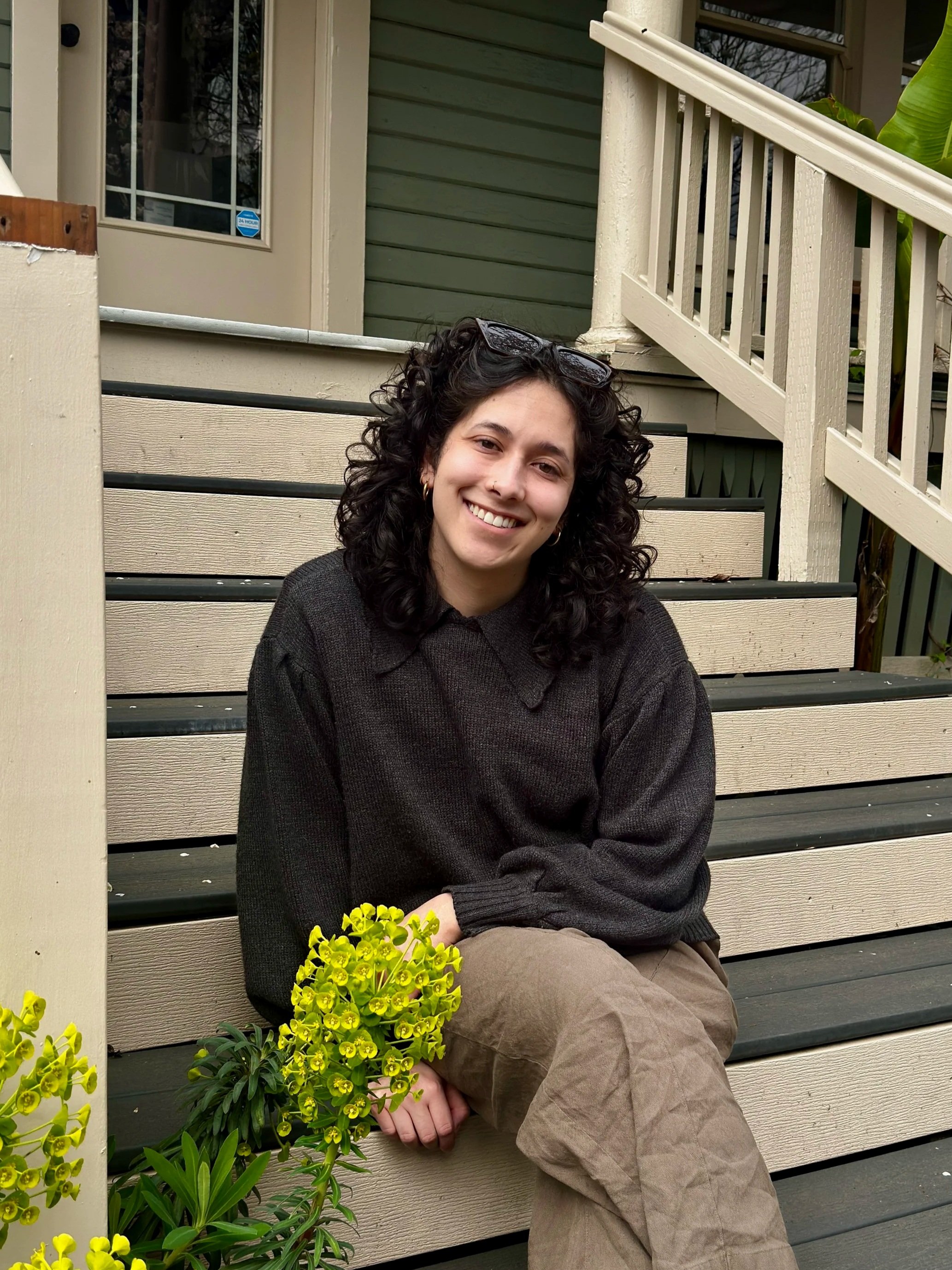 Kai Leyva, curl specialist at Gilded Fox, smiling against a brick wall, Portland Oregon curly hair salon