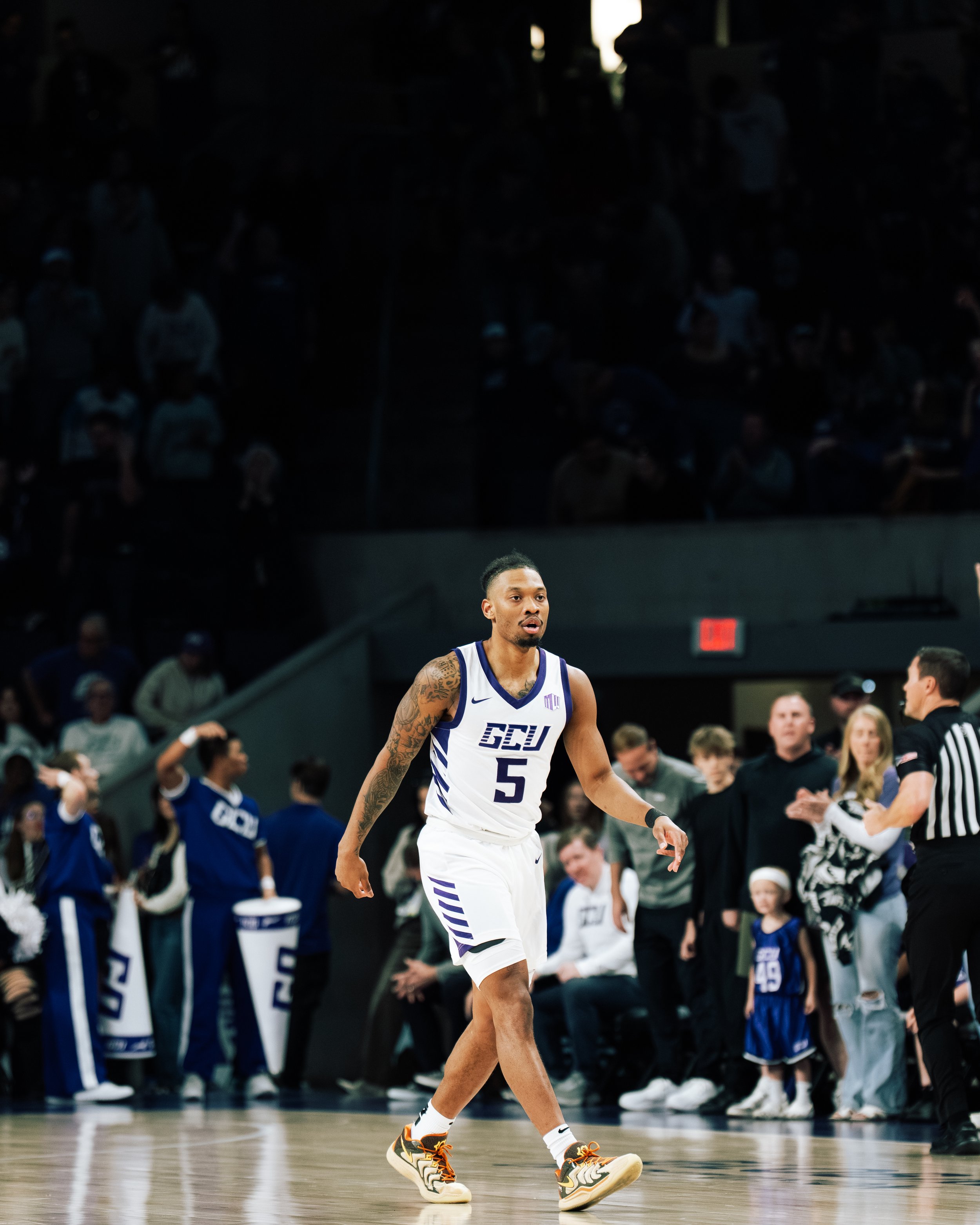 A Georgetown Hoyas basketball player wearing jersey number 5 walking on the court during a game, with cheerleaders and spectators in the background.