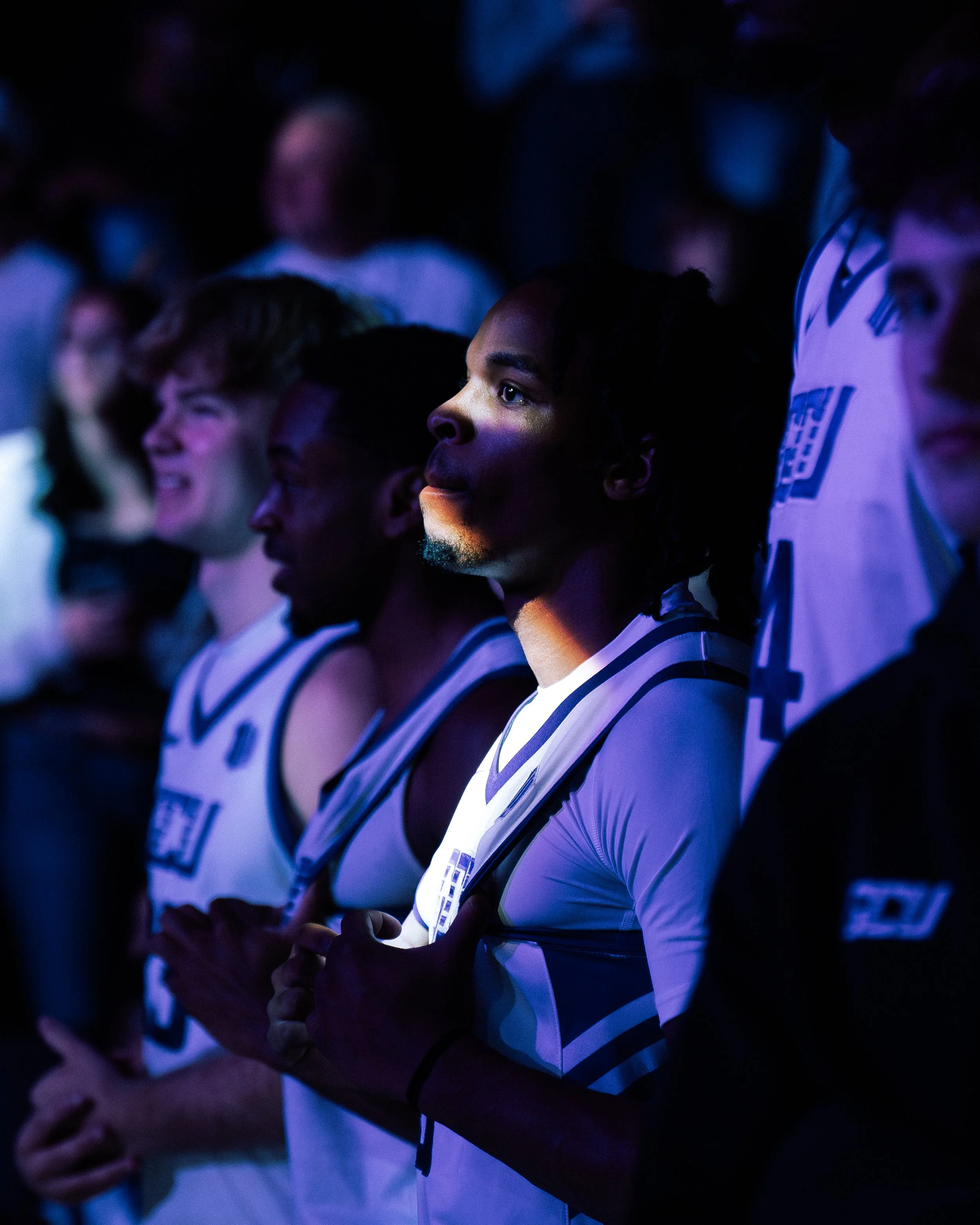 A group of basketball players standing with their hands over their hearts, focused on the national anthem during a game or ceremony.