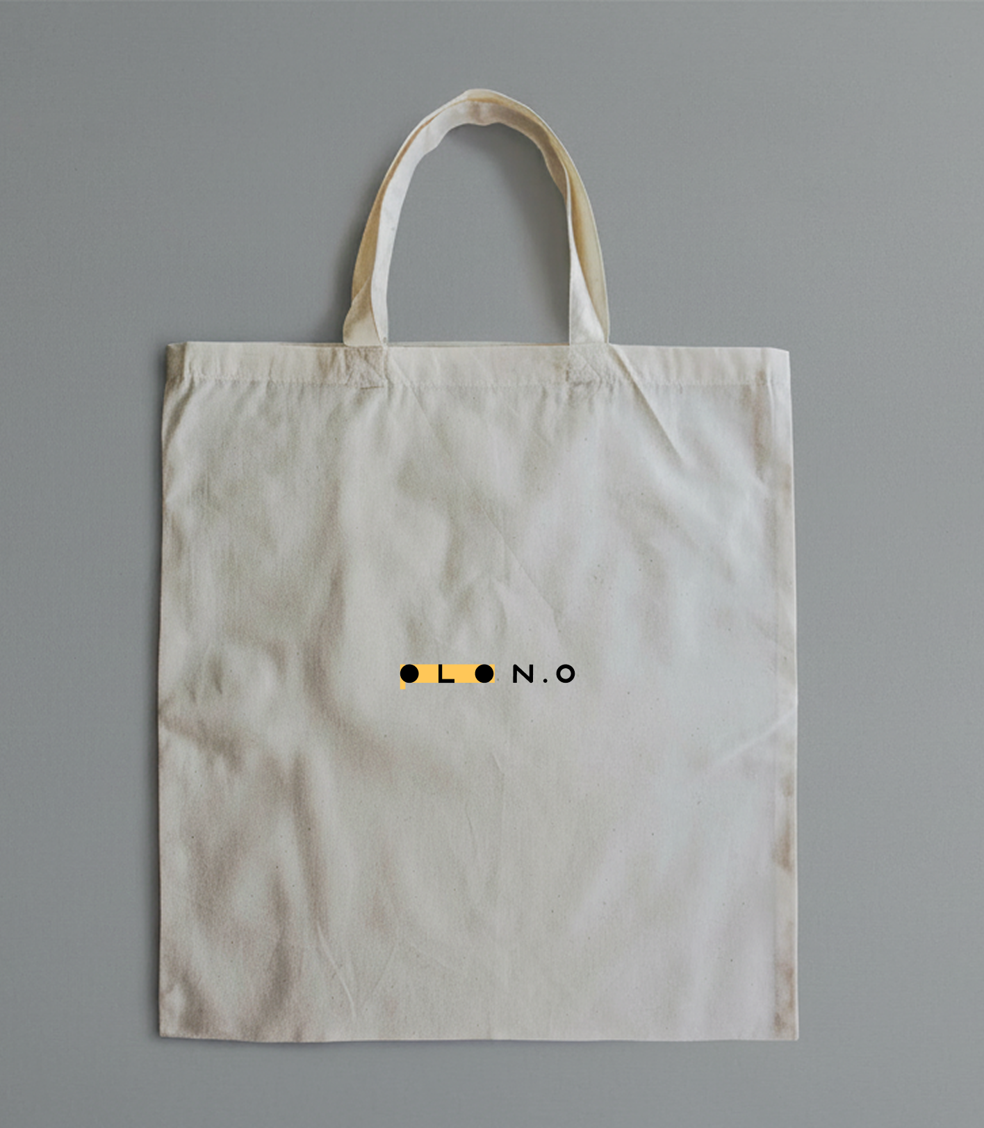 A white tote bag with a small graphic design and the text 'O L N.O' printed on it, lying on a grey background.