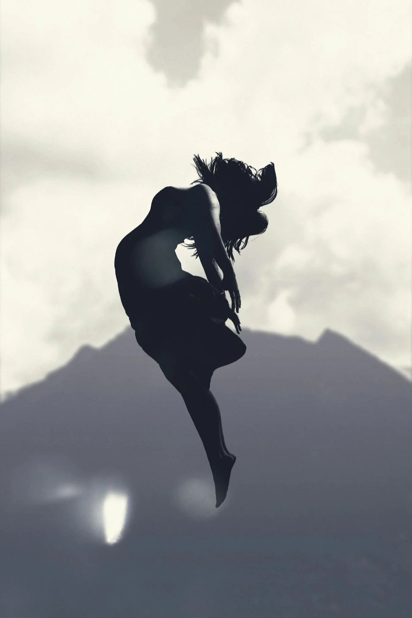Silhouette of a person with long hair jumping or dancing against a cloudy sky.