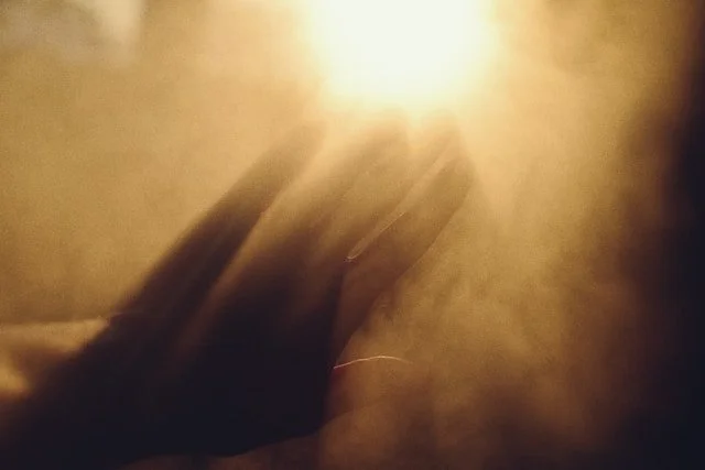 A blurry, abstract image with a hand reaching towards a bright, warm light source.