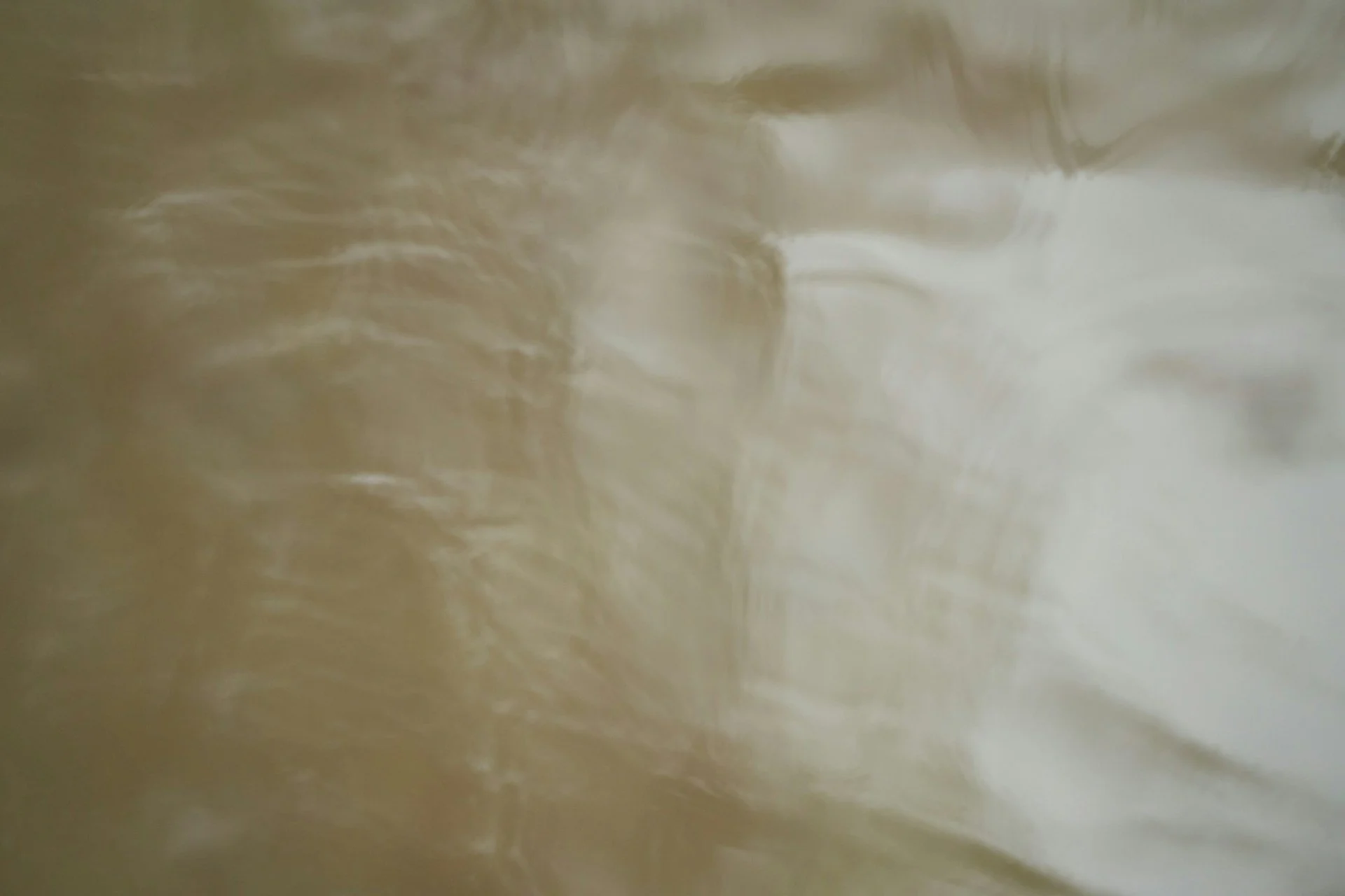 Close-up of a flowing, textured, golden-brown liquid or substance with ripples and reflections.