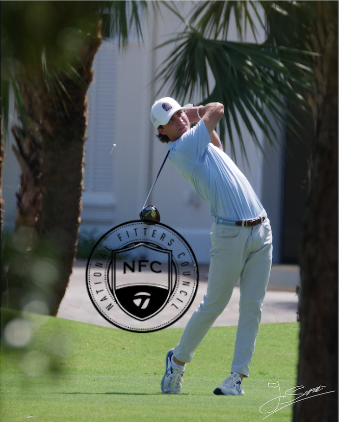 A woman playing golf on a lush green course, swinging a club with trees in the background.