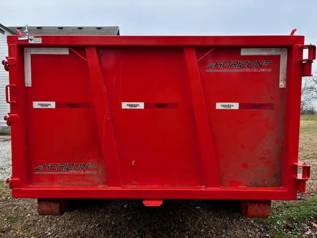 Red Horizon small dump trailer with black and white labels on the side, parked outdoors on a grassy or dirt area.