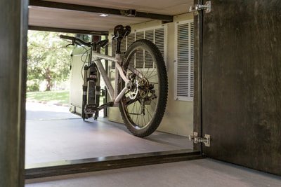 A bicycle inside a garage or storage space, with an open door showing greenery outside.