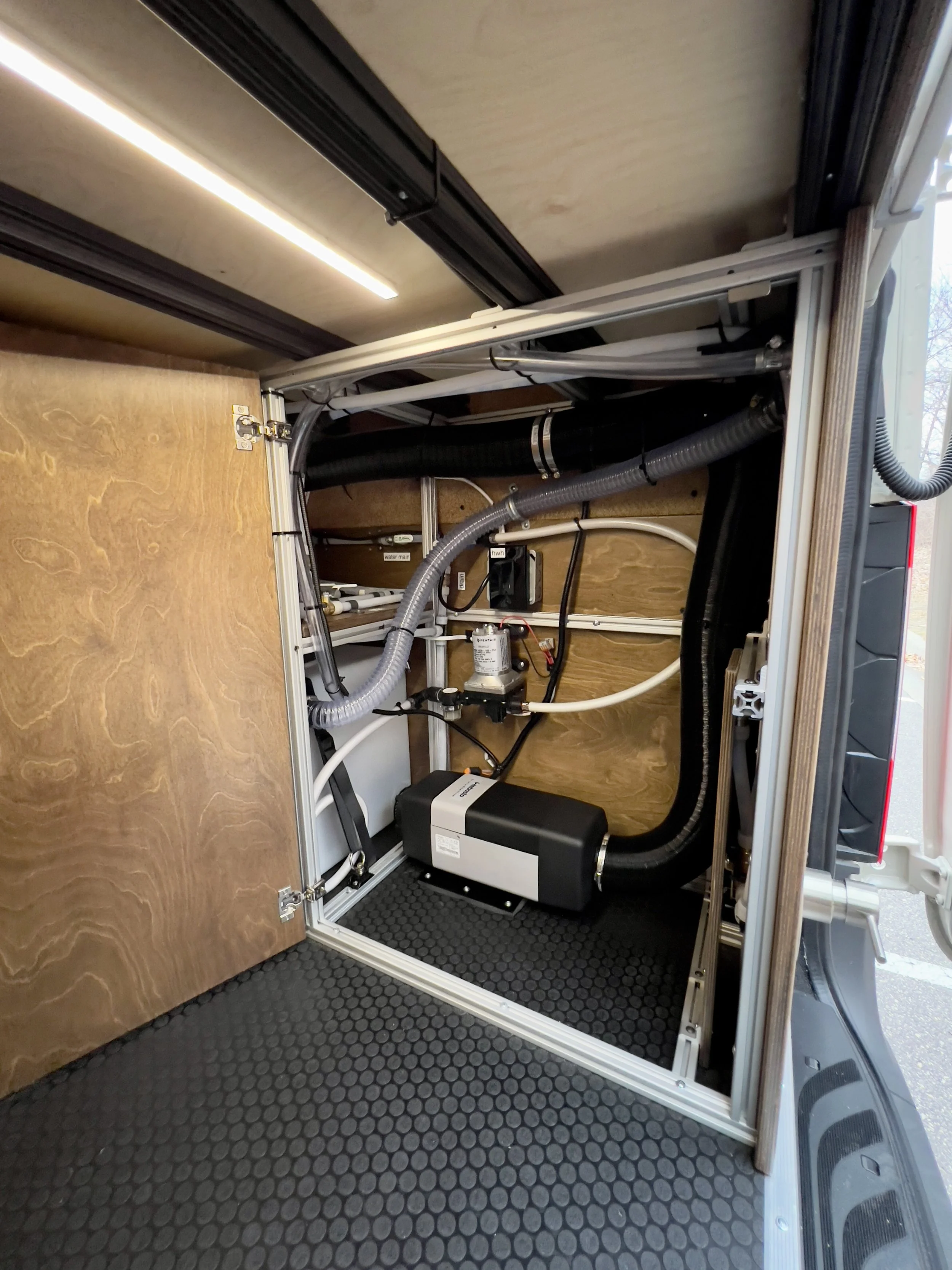 Open compartment of a mobile water filtration or pump system showing hoses, pumps, and wiring.