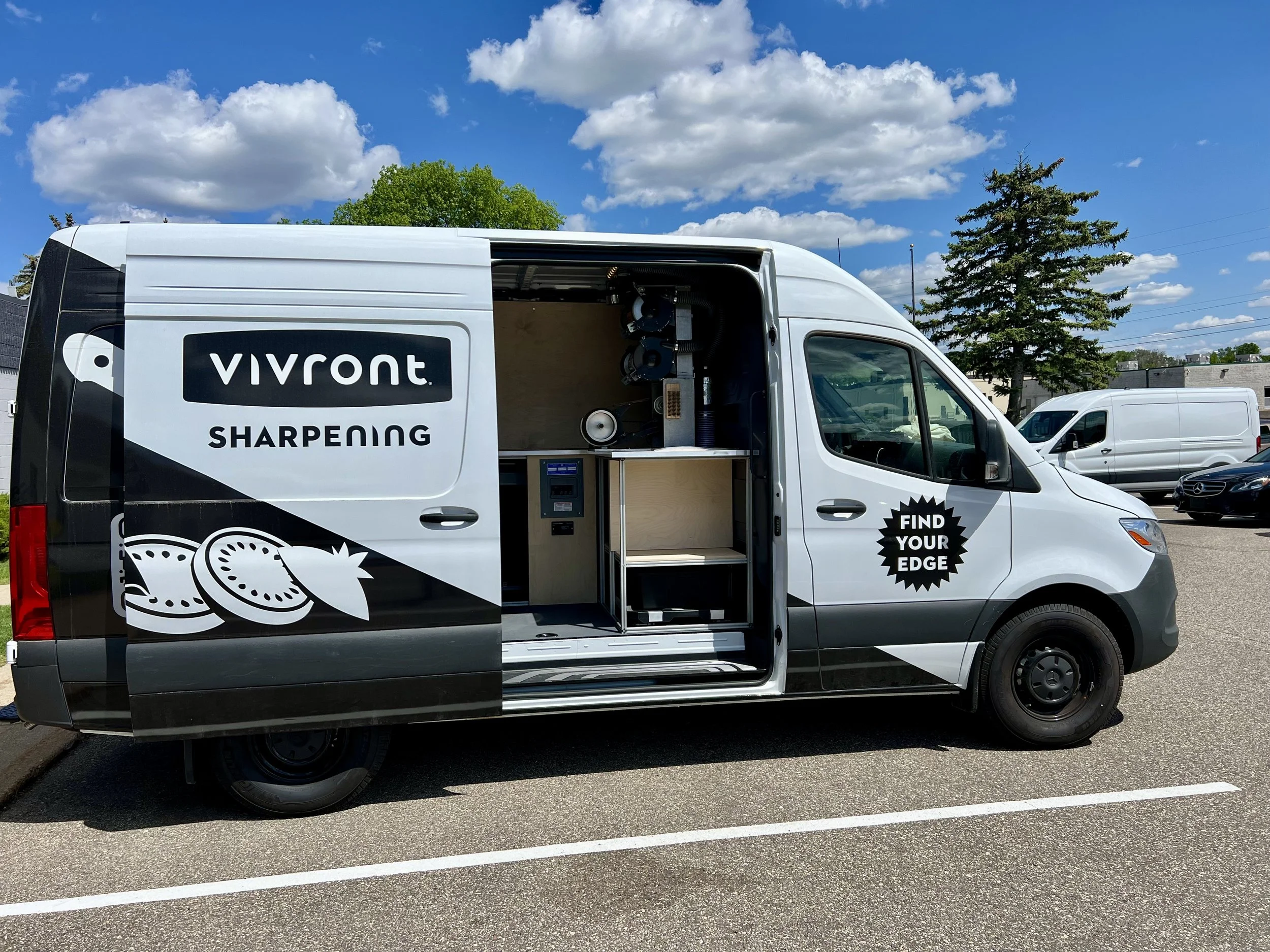 A mobile vending van with the branding 'Vivront Sharpening' and a tagline 'Find Your Edge,' parked in an outdoor lot with other vehicles, under a partly cloudy sky.