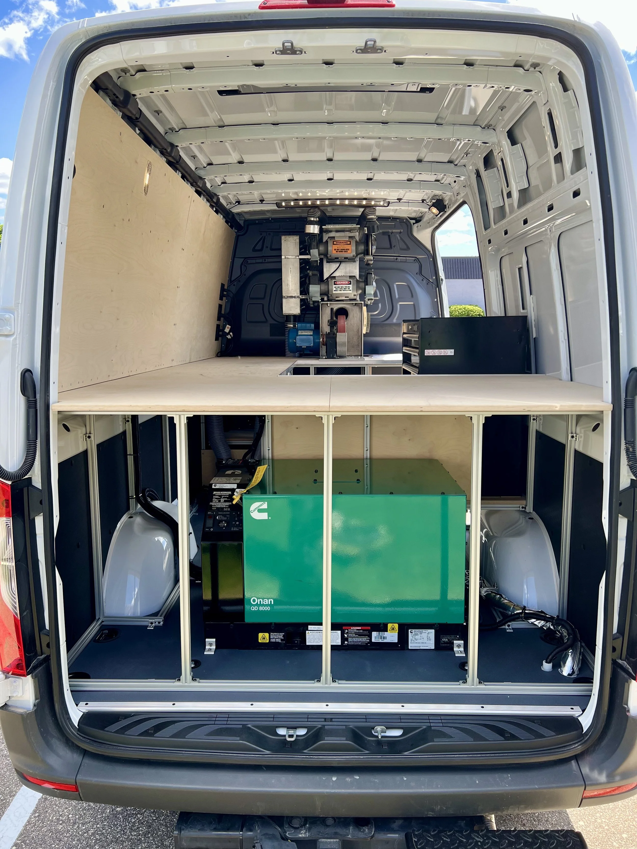 The back of a cargo van showing an electric vehicle charging system with batteries and equipment installed inside