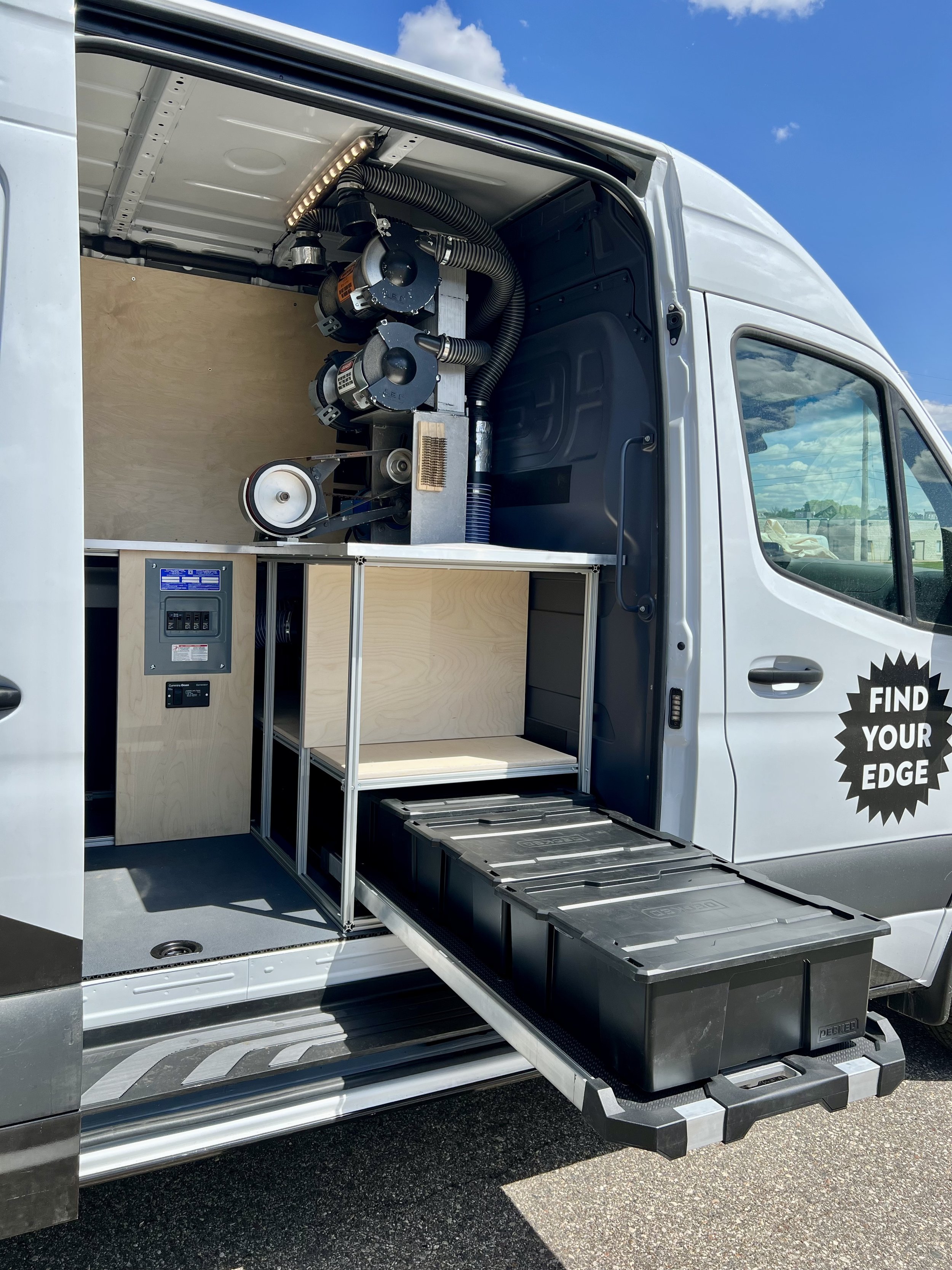 Interior of a service or utility van with equipment mounted on the wall, including vacuum or piping systems, and storage cabinets and containers at the back. The side door is open, revealing the setup inside.