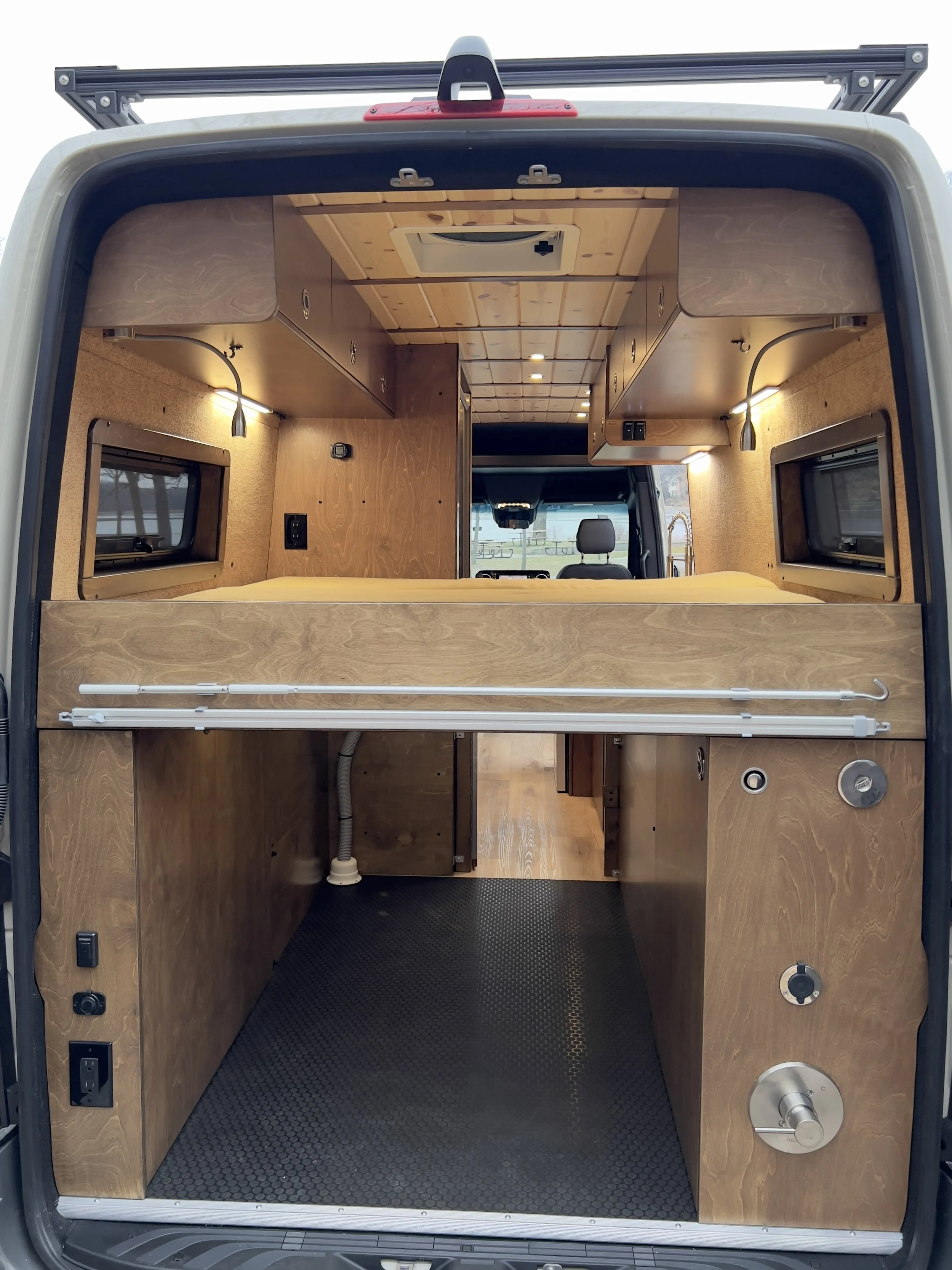 Interior of a converted van with wooden cabinetry, small windows, and a rubber flooring, designed for camping or mobile living.