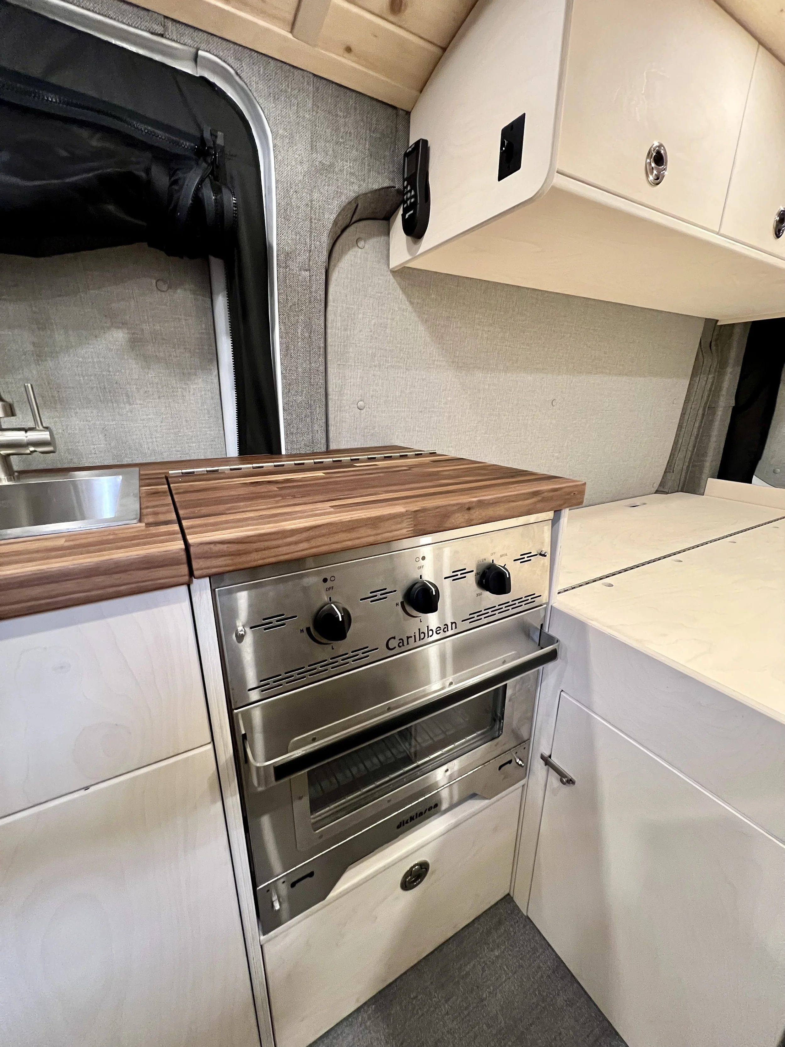 Small kitchen area with a countertop hardwood surface, a stainless steel oven with three black control knobs, white cabinets, a stainless steel sink, and a black remote control on the countertop.