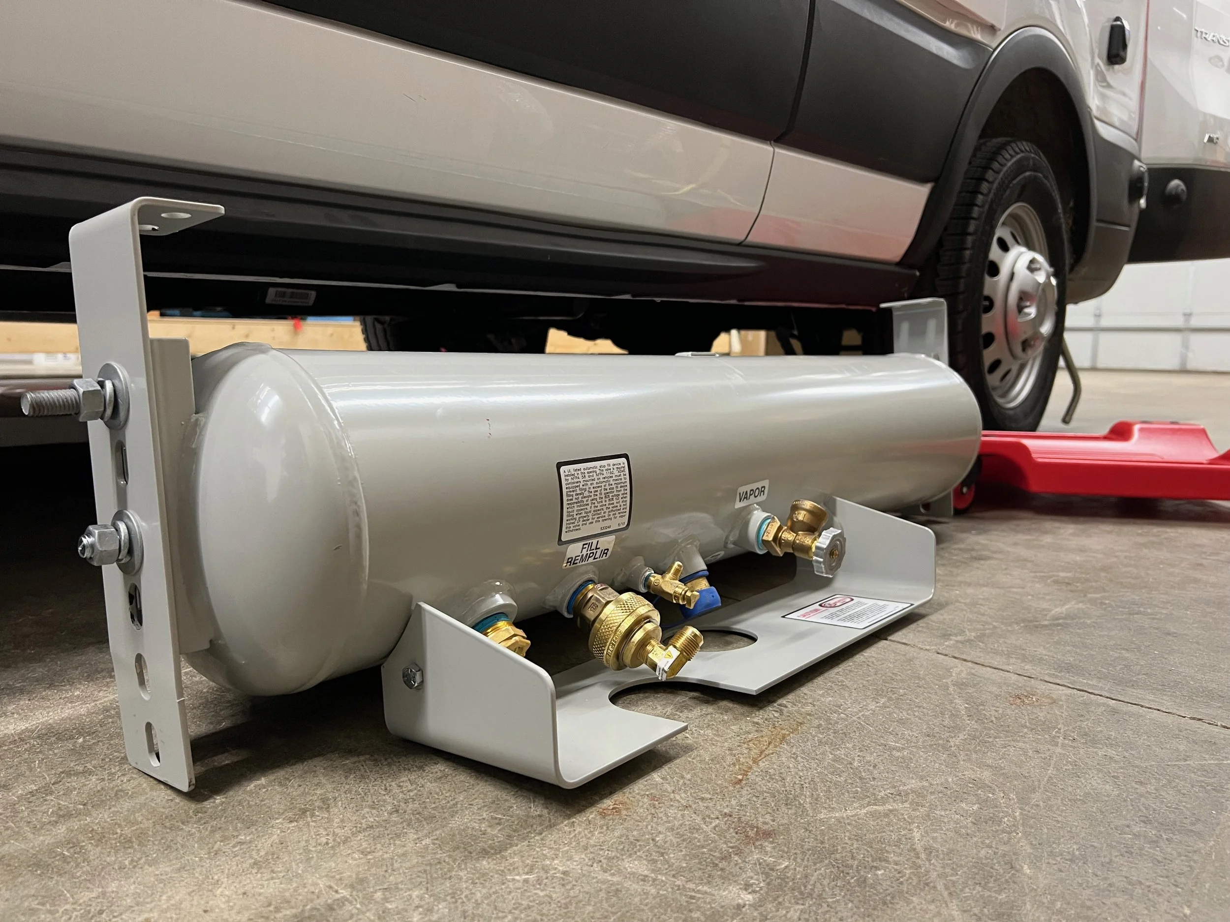 A propane tank installed under a vehicle in a garage, with the garage door and part of the vehicle visible.