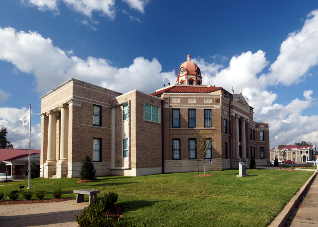 A historic courthouse with a domed roof in a city setting, surrounded by a well-maintained lawn and sidewalk, under a partly cloudy sky.