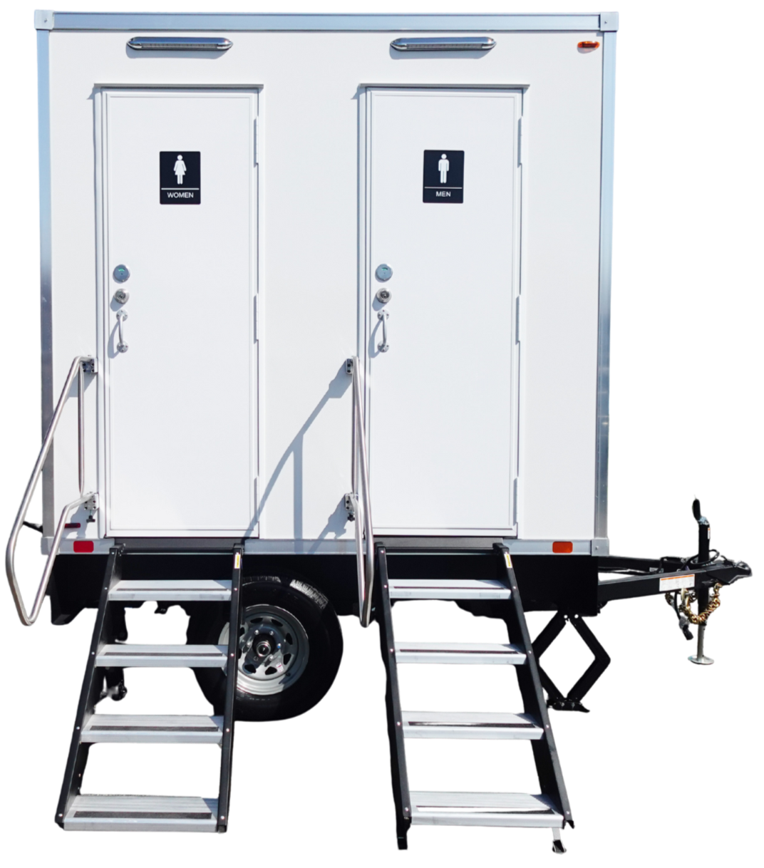 A portable restroom trailer with separate doors for women and men, accessed by metal stairs. Bathroom signs are visible on each door.