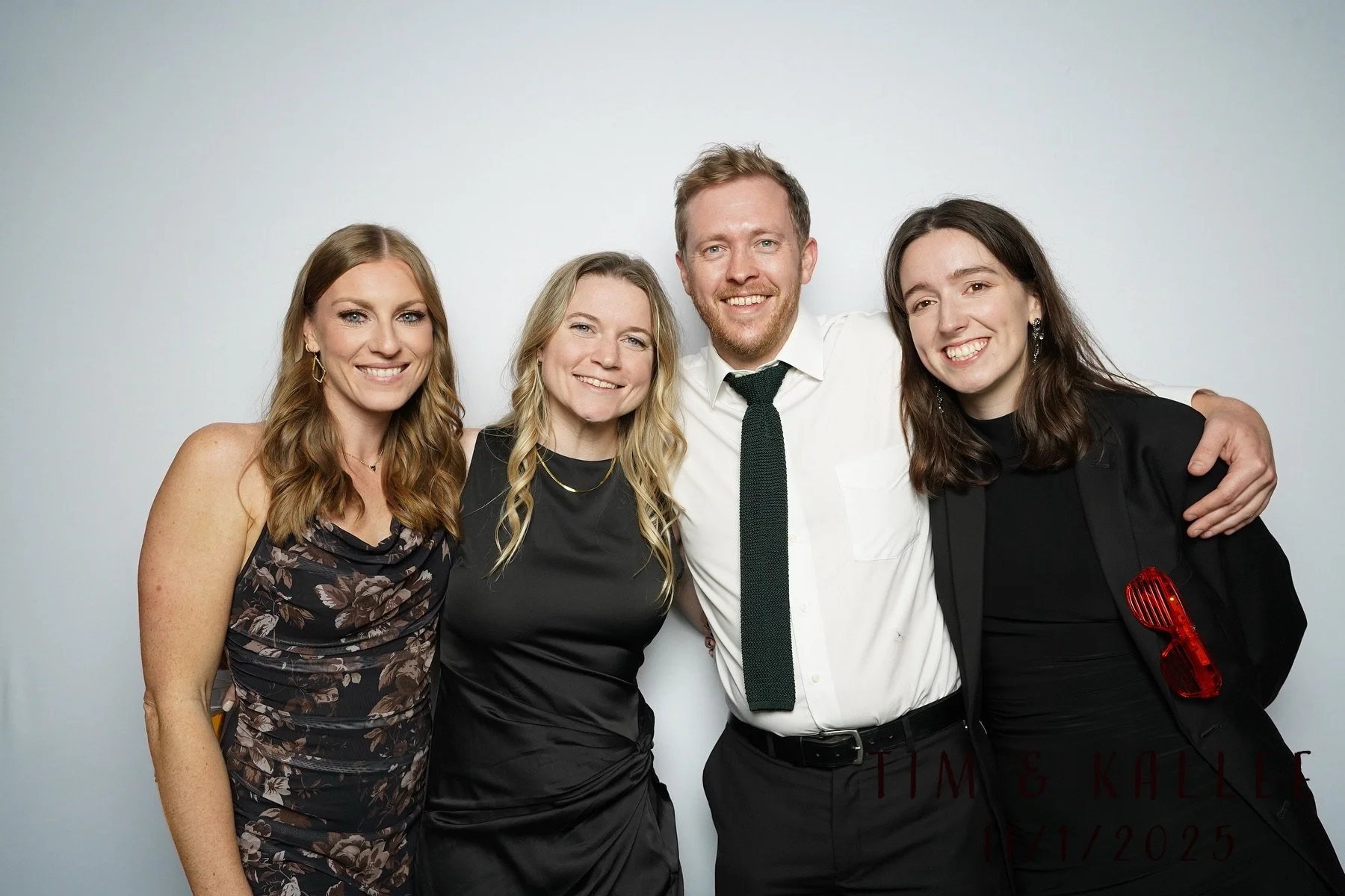 Four people standing together in formal attire, smiling, against a plain white background.