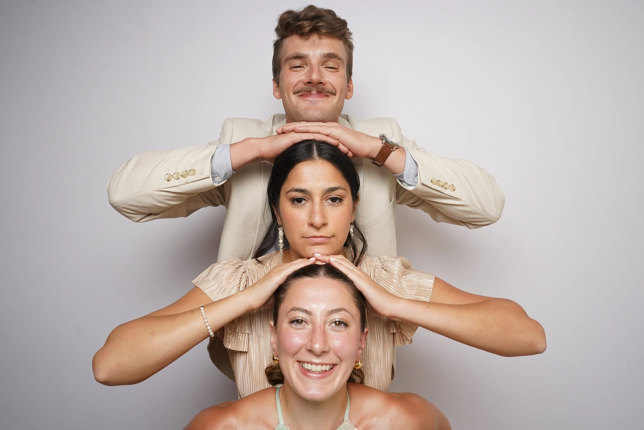 Three people stacked in a pyramid pose, each with hands on the head of the person below, smiling and looking at the camera.