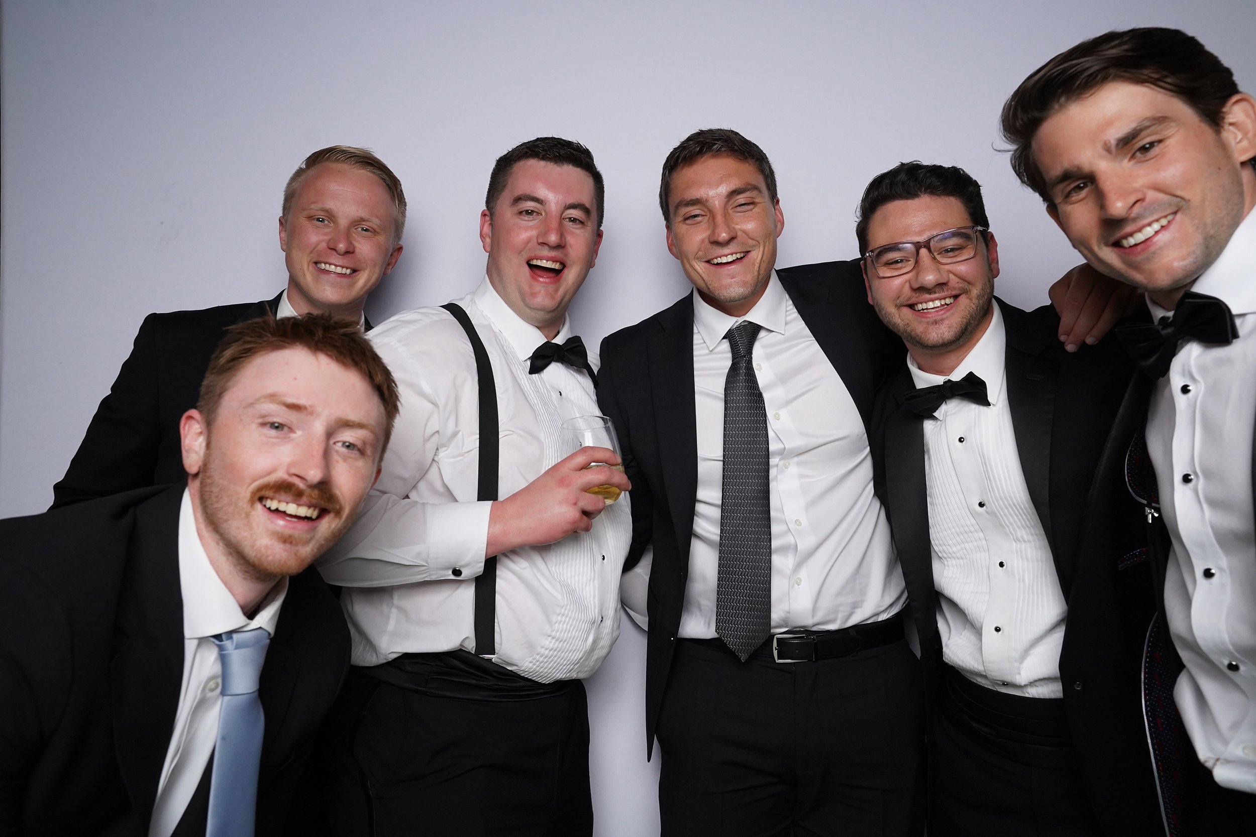 Group of seven men in formal attire smiling, posing together at a social event.