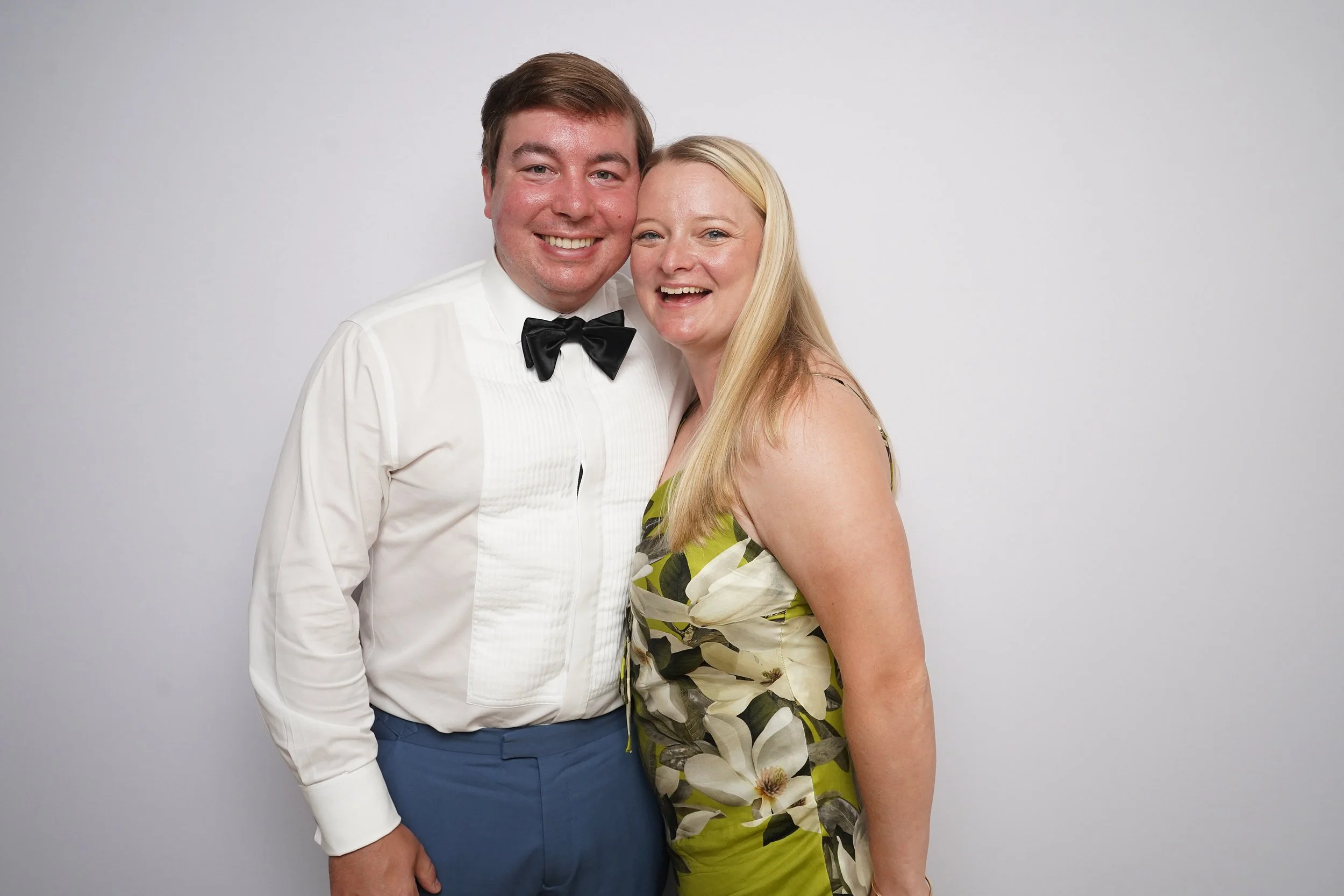 A smiling couple dressed in formal attire, standing close together against a plain white background.