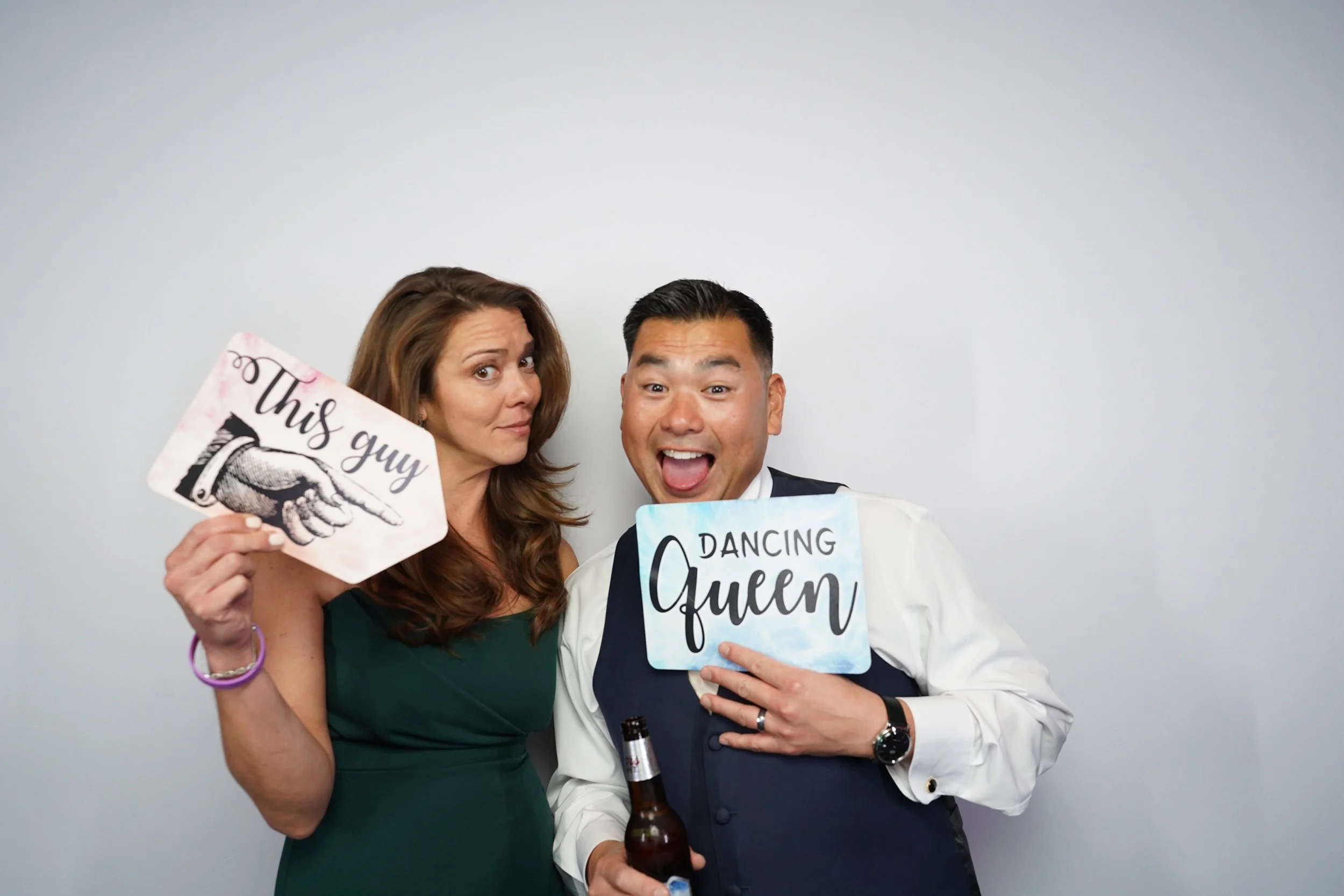 A woman holding a sign that says "This guy" pointing at a man who is holding a sign that says "Dancing Queen" while smiling and posing for a photo.