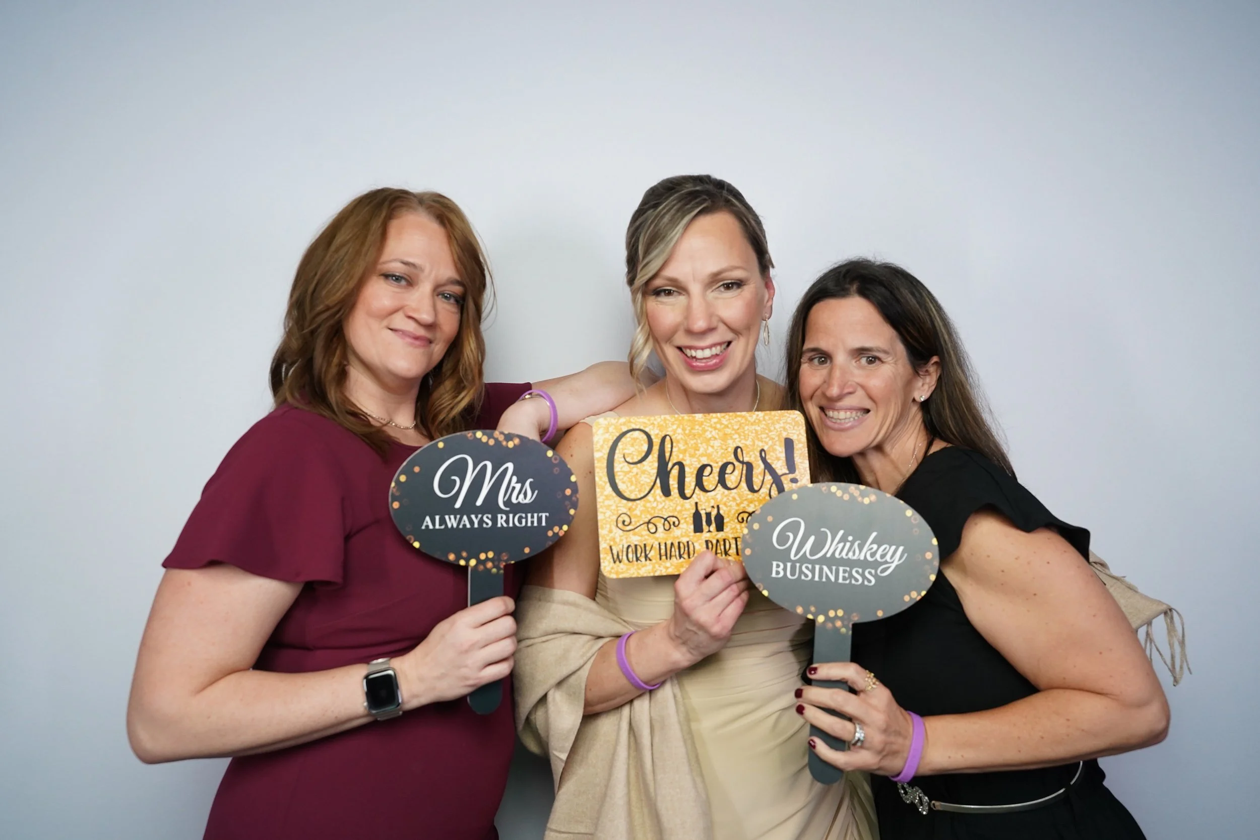 Three women holding signs at a celebration, smiling and posing for the camera