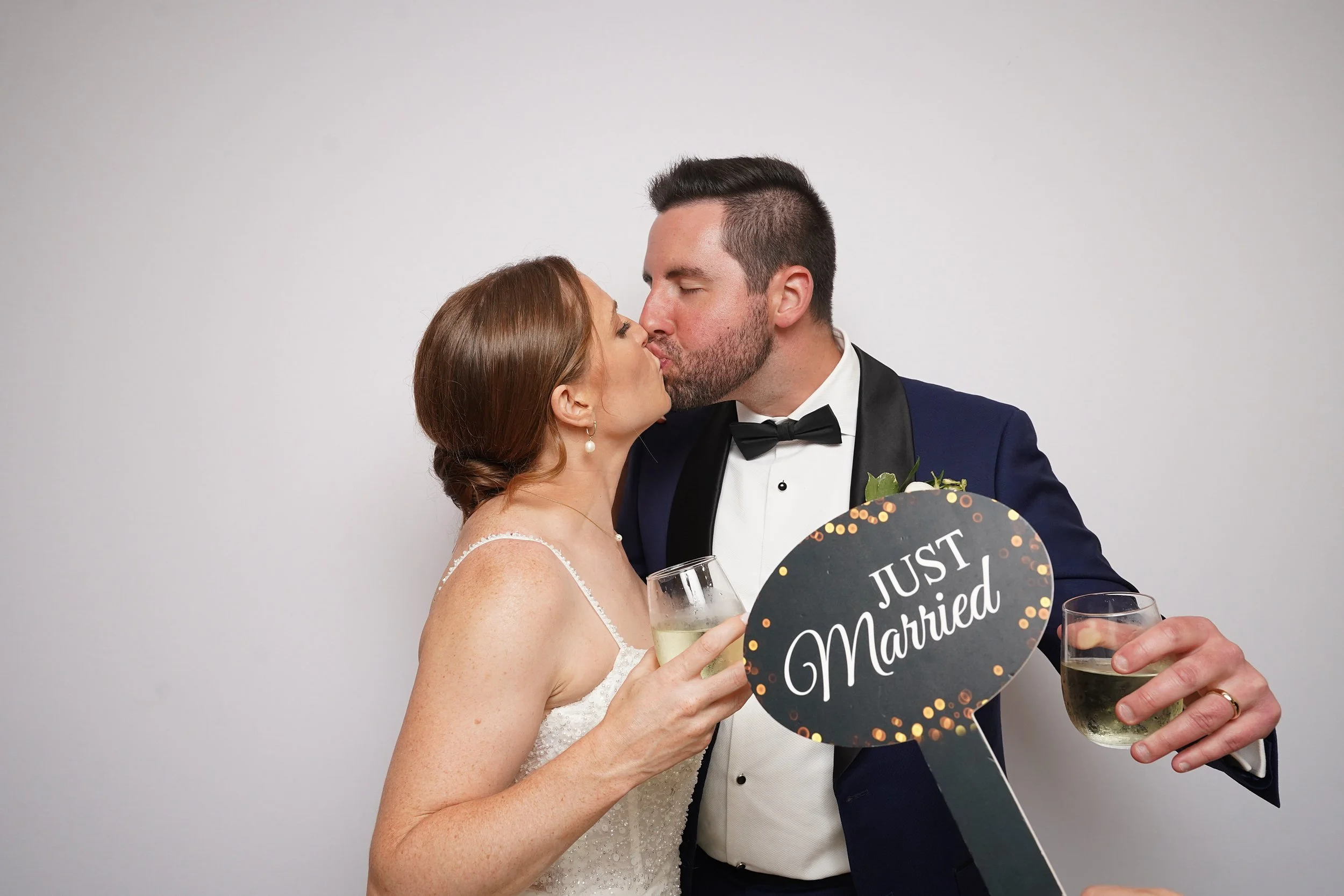 A newlywed couple kissing at their wedding reception, holding glasses of champagne, with a 'Just Married' sign.