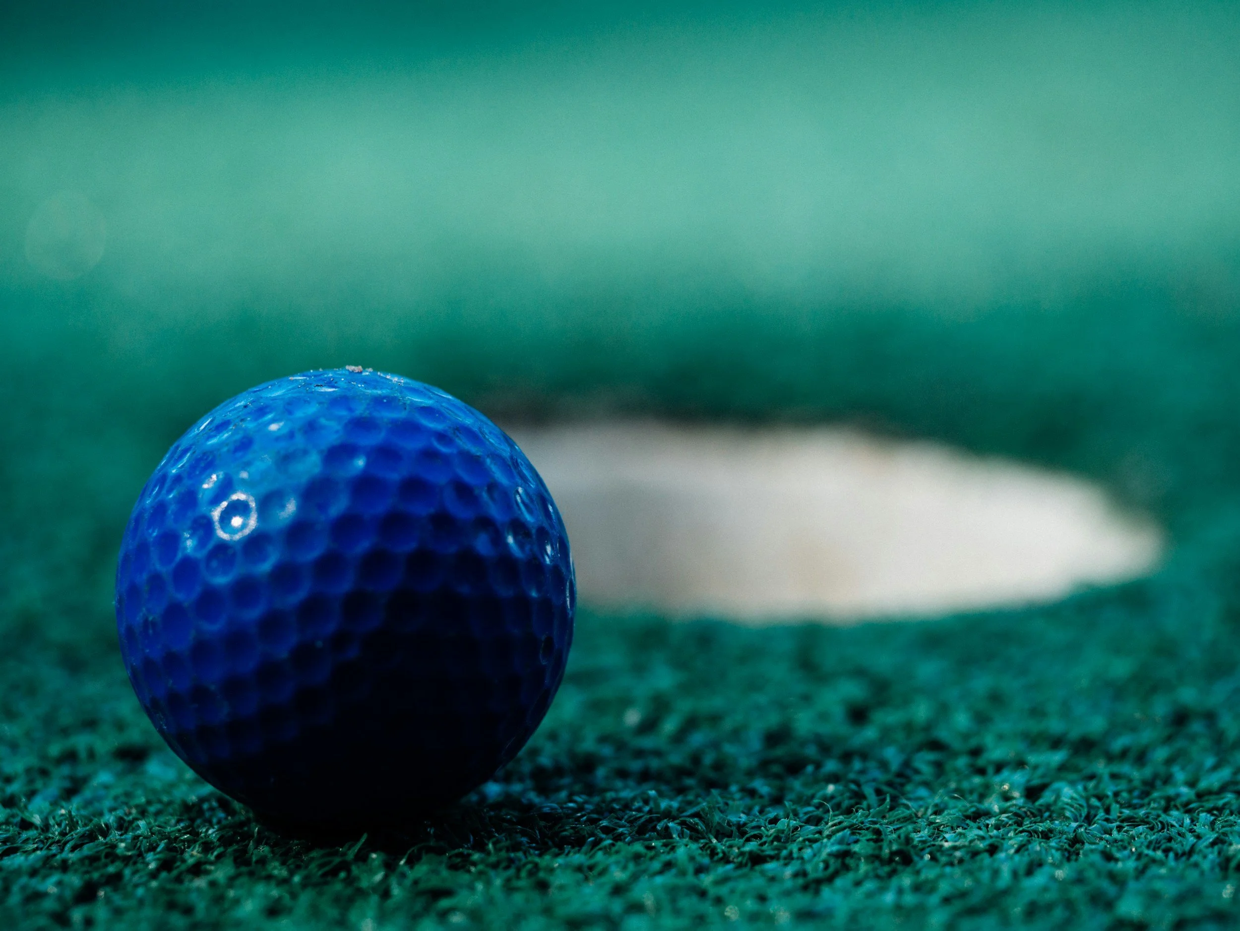 Close-up of a blue golf ball on a green golf course with a white hole flag in the background.