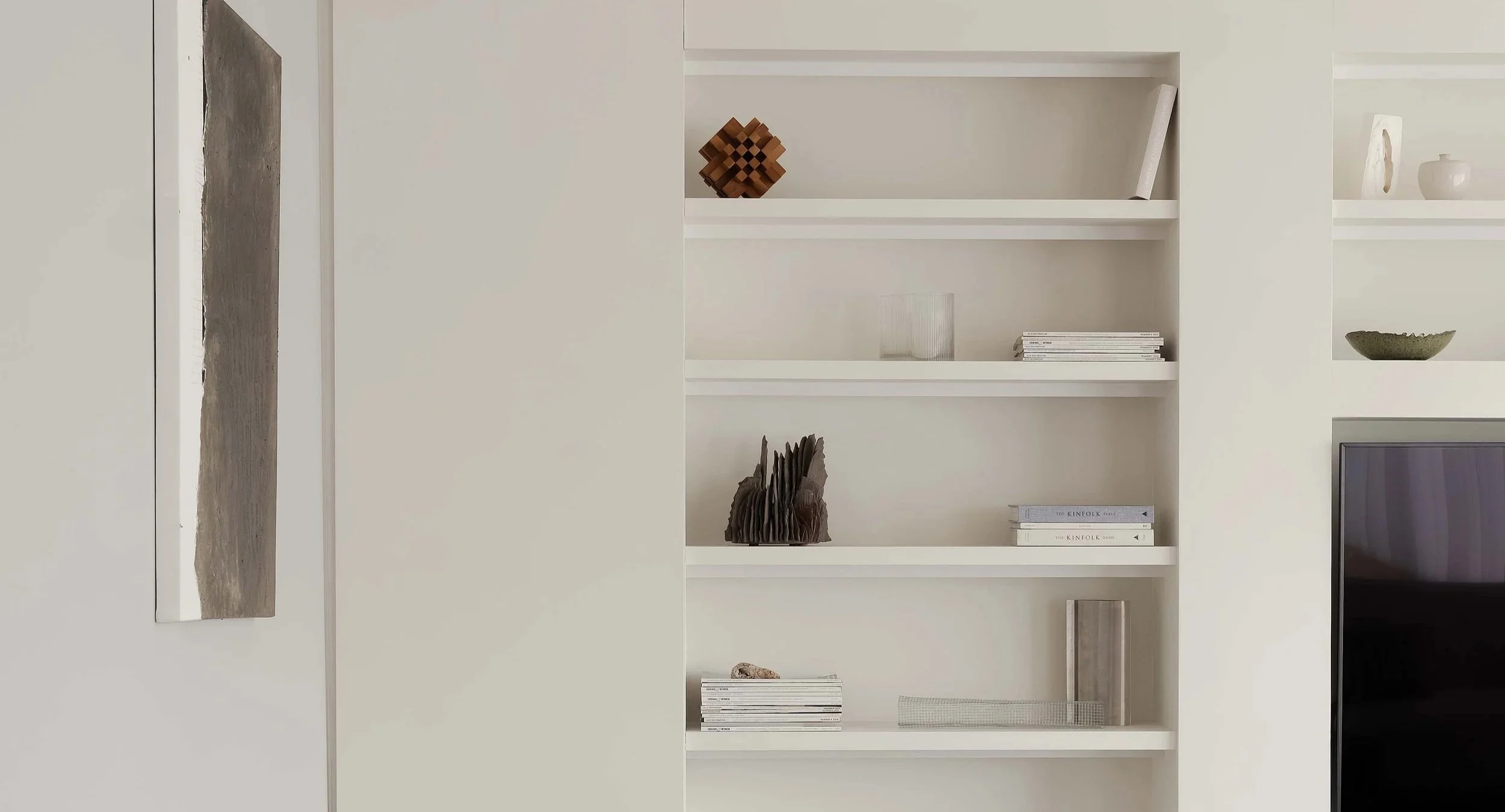Interior Design project in Waterlooplein, Amsterdam. White built-in bookshelf with decorative items including books, sculptural objects, and vases in a modern living space.