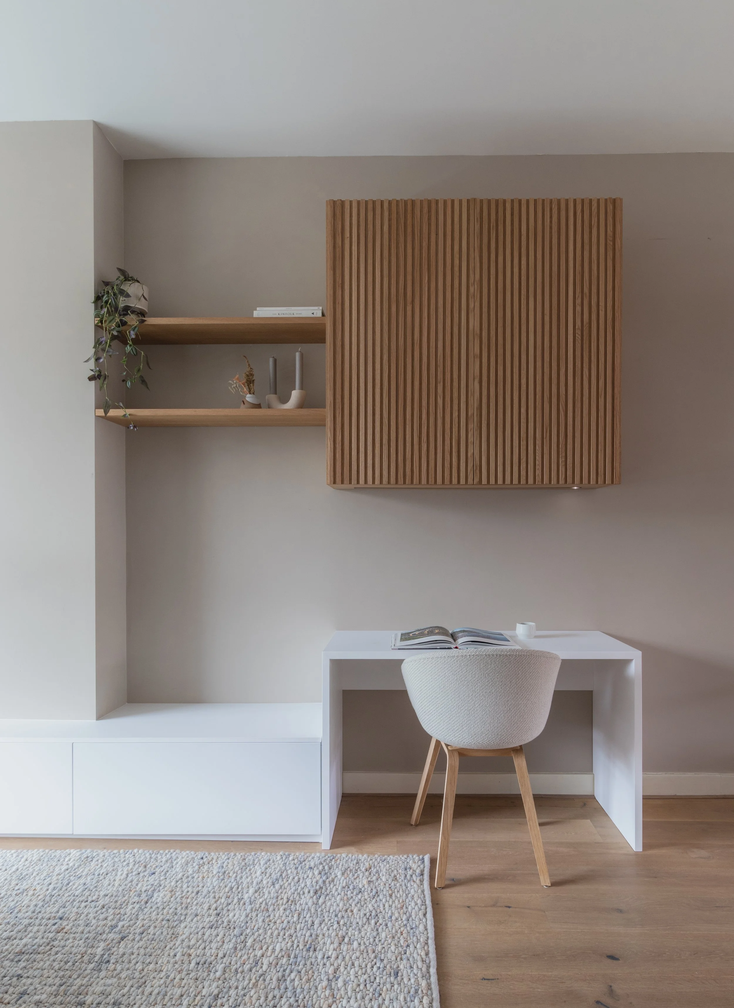Minimalist home office with white desk, gray upholstered chair, wooden shelves, and a textured beige rug.