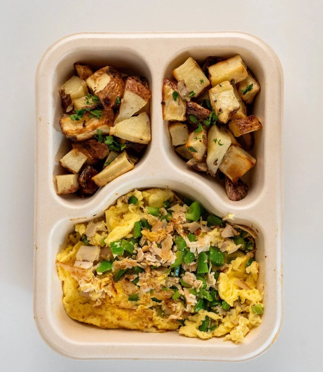 A compartmentalized tray with roasted diced potatoes topped with herbs, scrambled eggs with green onions and shredded chicken.