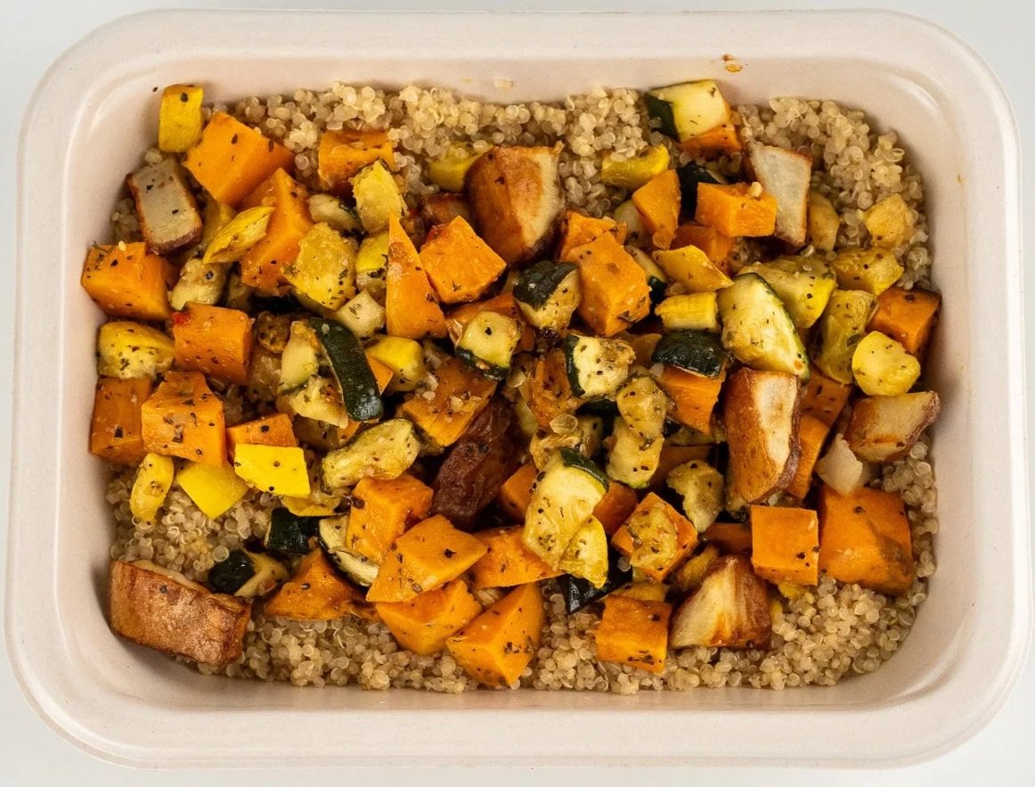 Roasted vegetables served over cooked quinoa in a rectangular container.