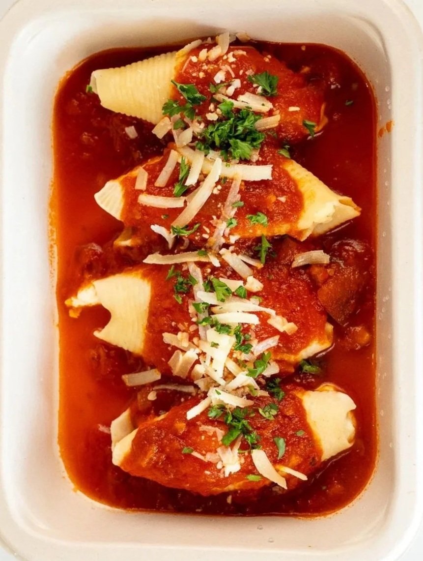 Baked stuffed pasta shells topped with marinara sauce, shredded cheese, and chopped parsley in a white casserole dish.