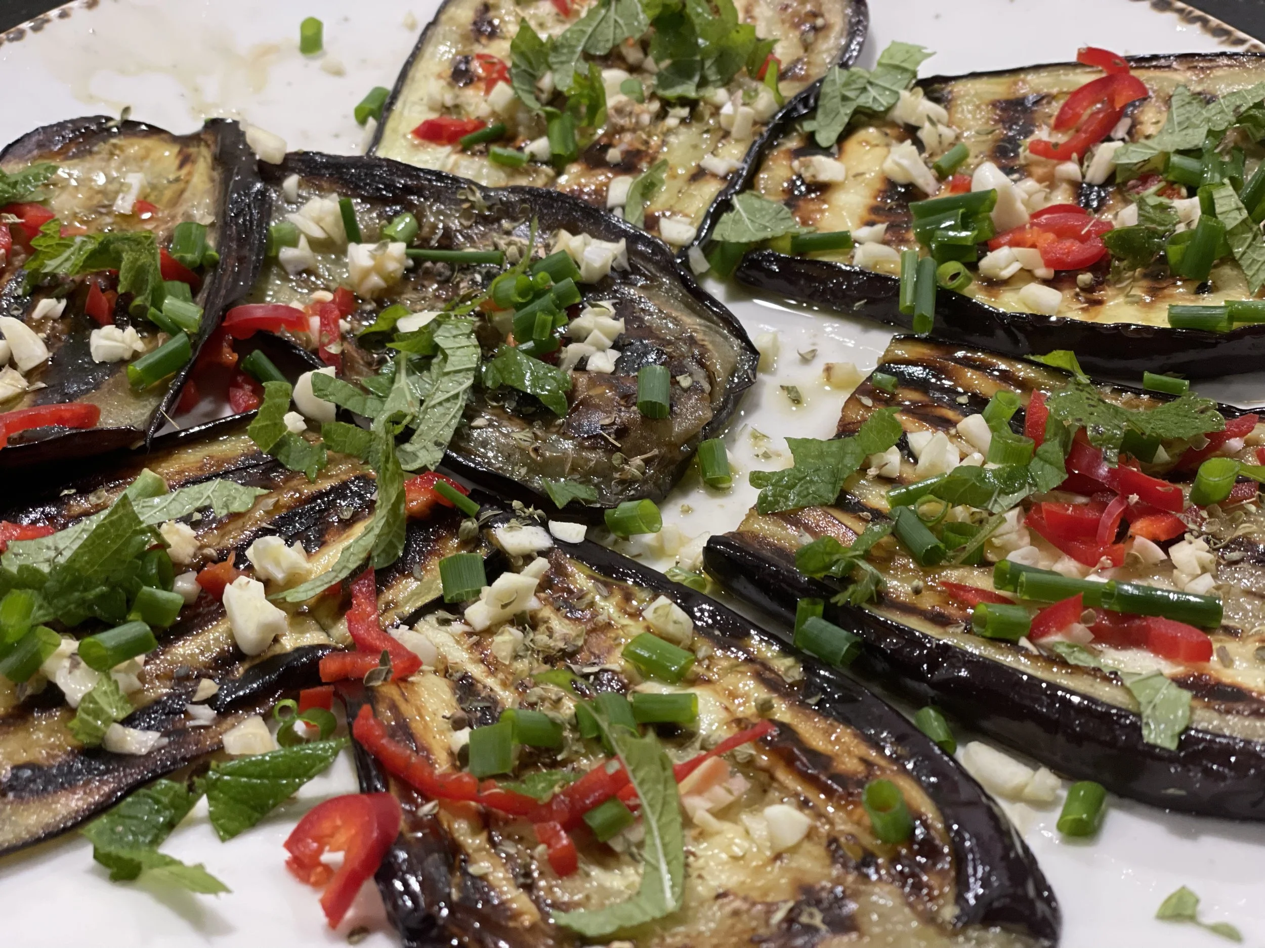 Gegrillte Auberginenscheiben mit gehacktem Knoblauch, roten Paprika, frischen Kräutern und Zwiebeln