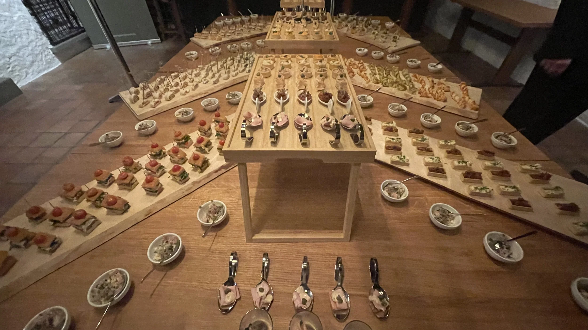 Vielfältige und kleine Häppchen auf Holzplatten und in Schälchen, präsentiert auf einem Holztisch für einen grossen Anlass mit 70 Personen