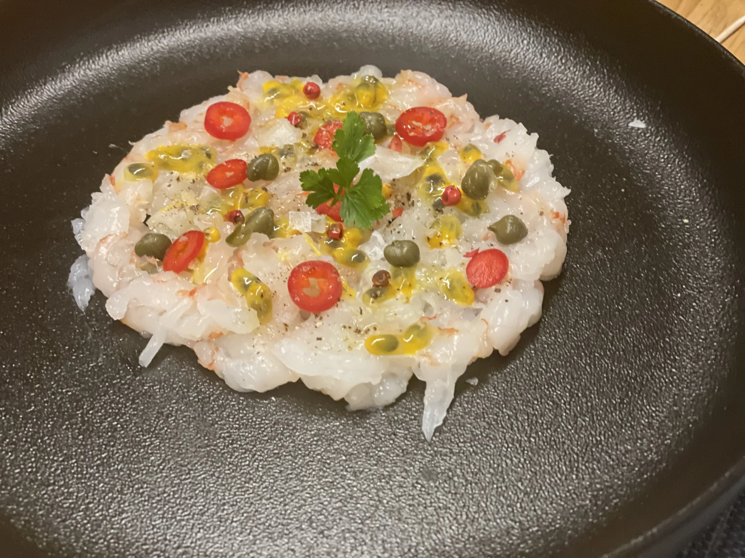 Rohe Garnelen bzw. Crevetten mit roten Pfefferkörnern, grünen Kapern, Tomatenscheiben, Zitronensaft und Koriander.