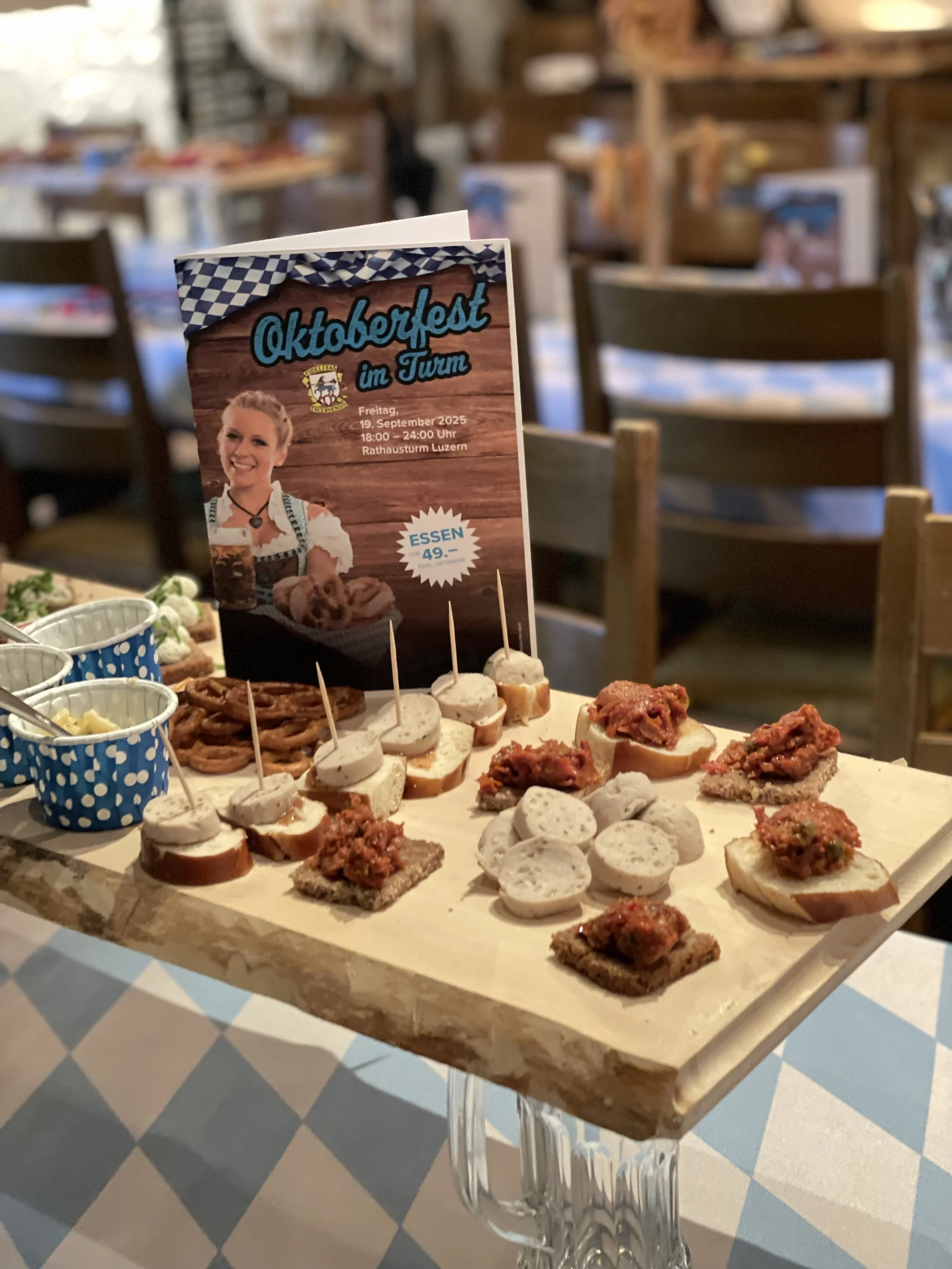 Auf einem Holzbrett sind verschiedene herzhafte Snacks wie kleine belegte Brote, Weisswürste, und Brezen. Alles für das Oktoberfest der Fidelitas in Luzern.
