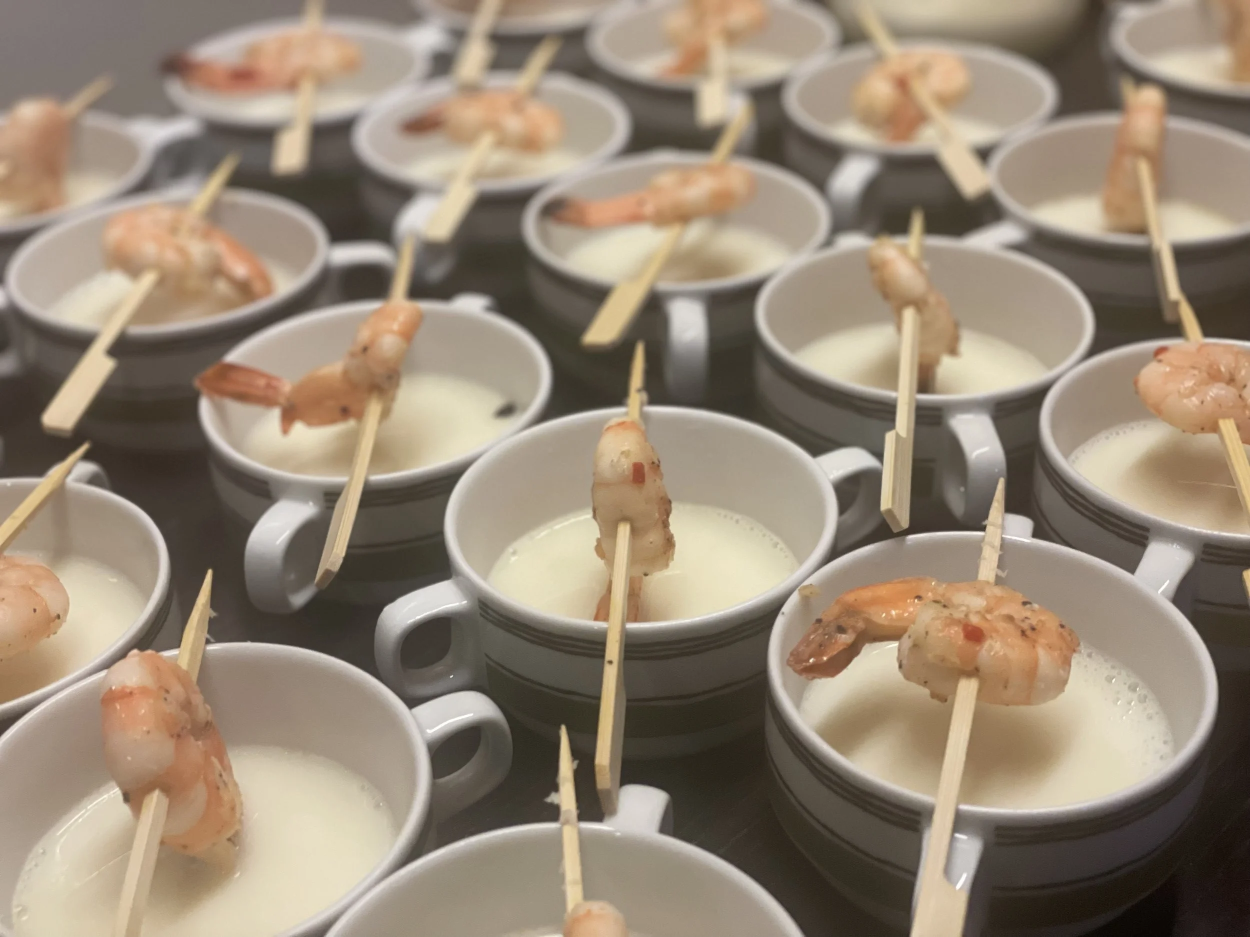 Mehrere weisse Tassen mit Suppen, Garnelen und Holzspiessen.
