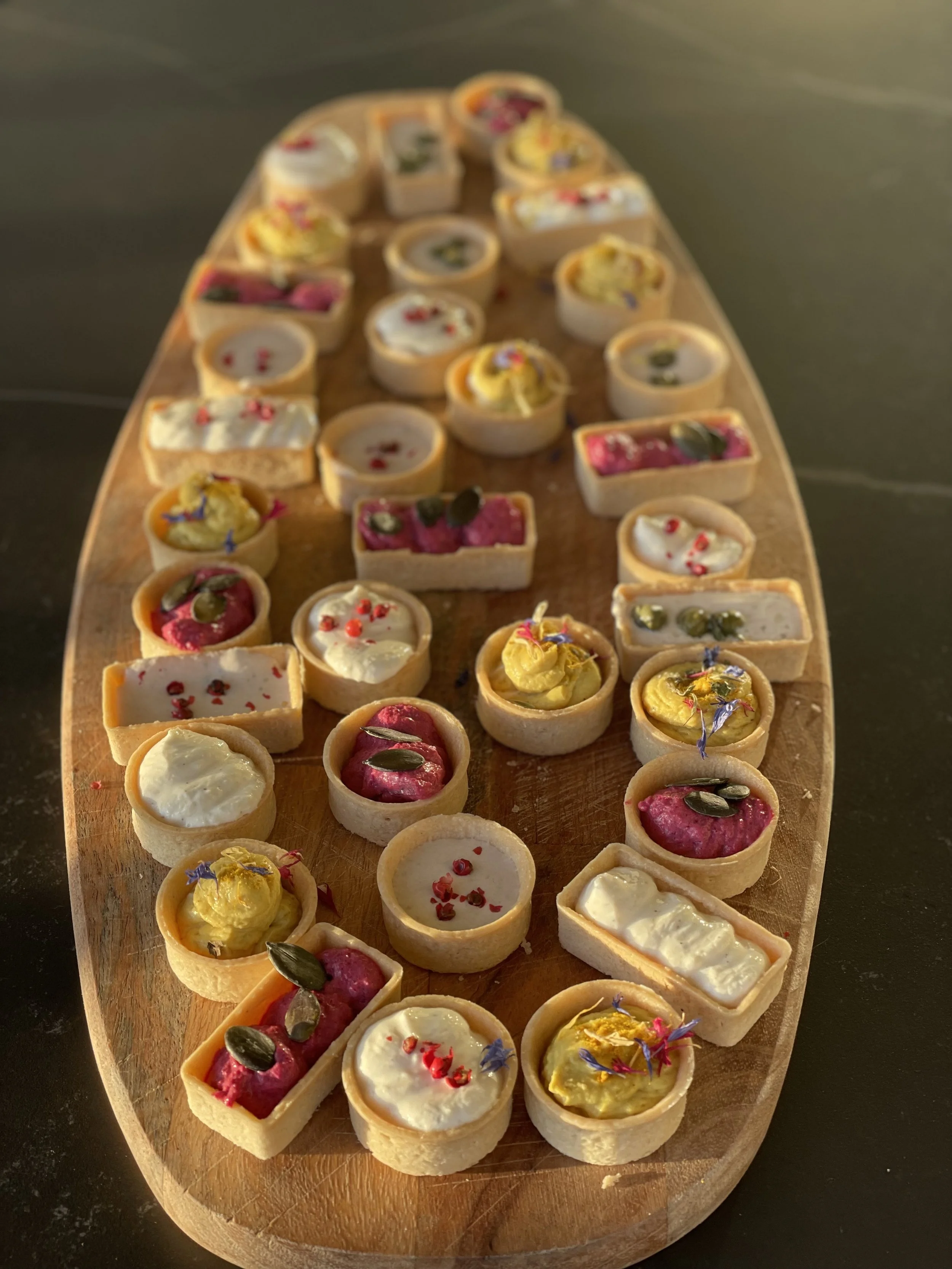Verschiedene kleine Tartelettes auf einem Holzbrett, dekoriert mit Blumen und Samen.