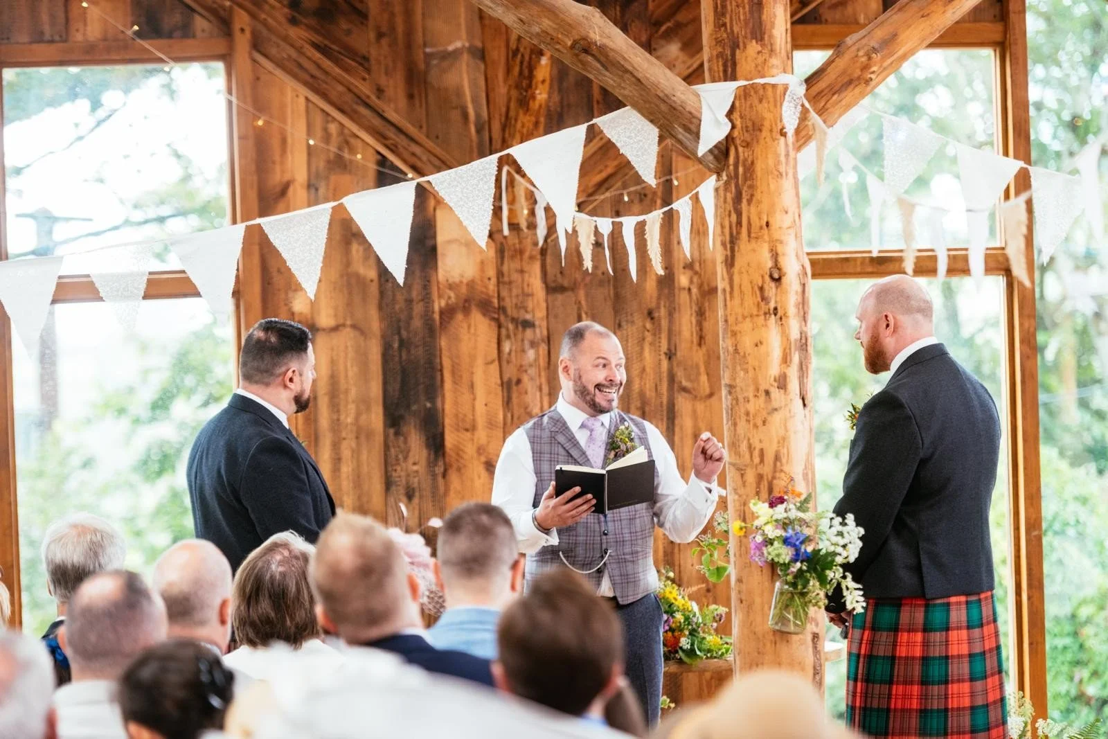 A wedding in a barn - the celebrant stands between two kilted grooms