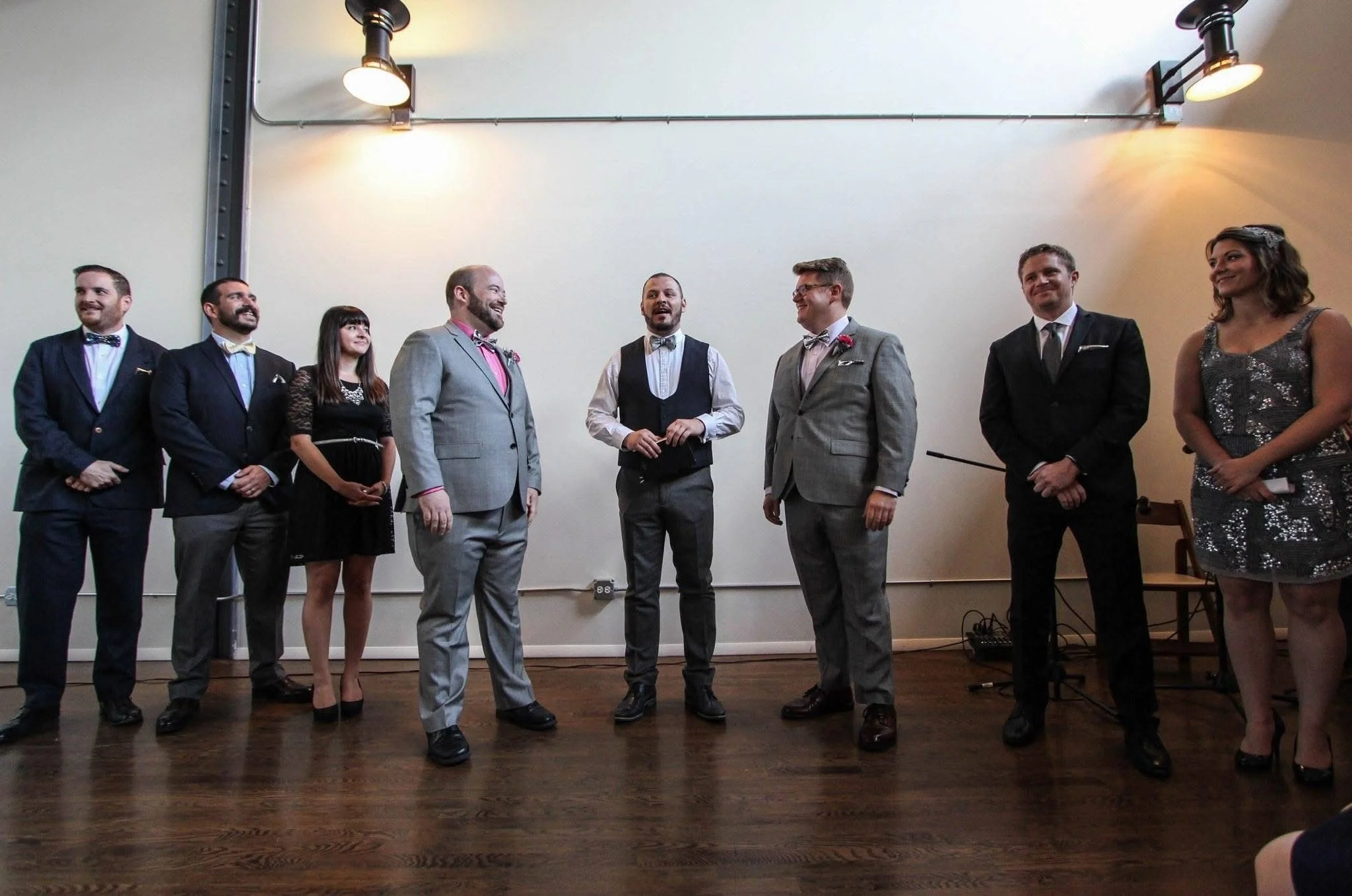 The celebrant is speaking to the audience, grooms at either side and surrounded by ushers and 'best people'