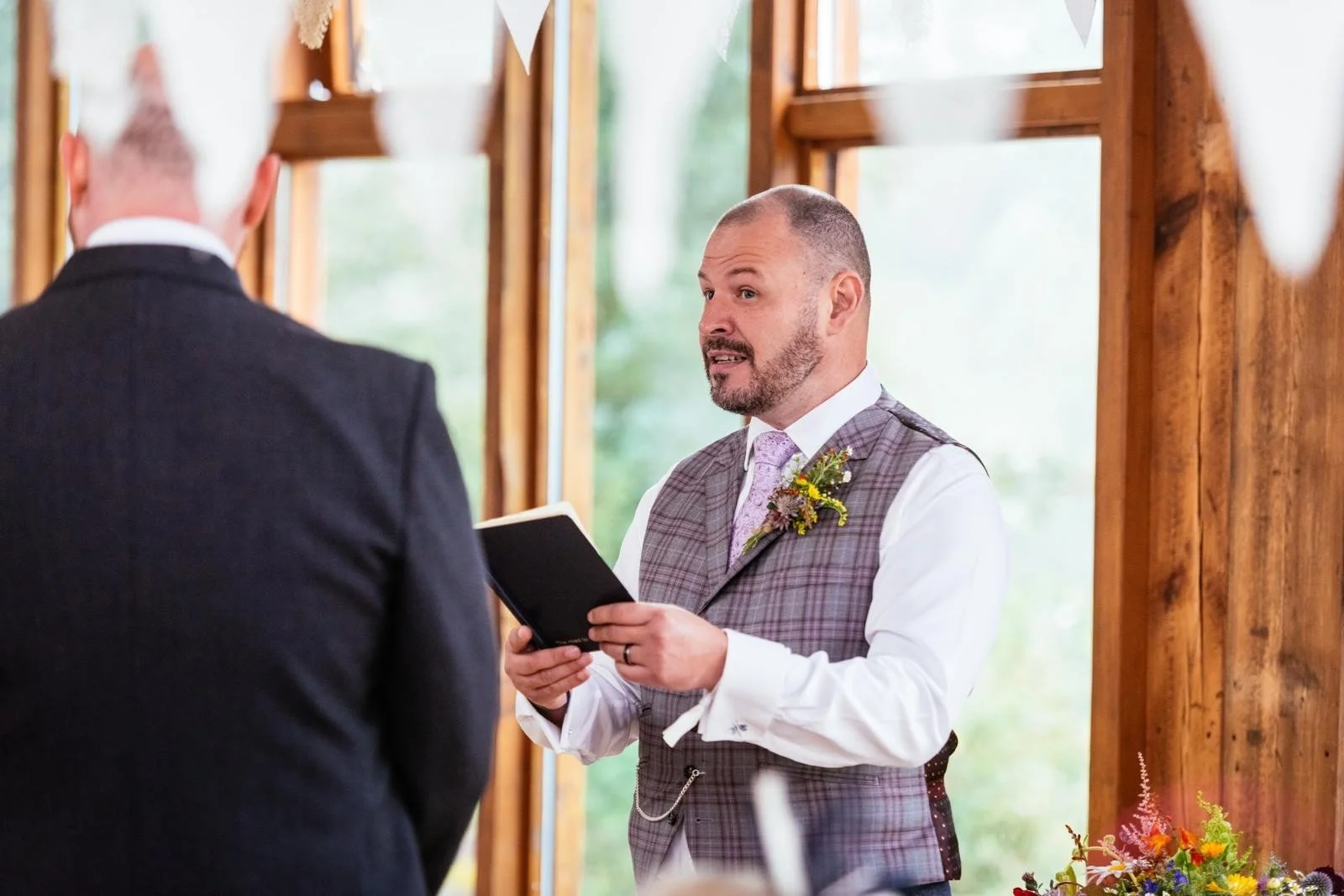 The celebrant looks up from his script, making eye contact with the couple just off camera