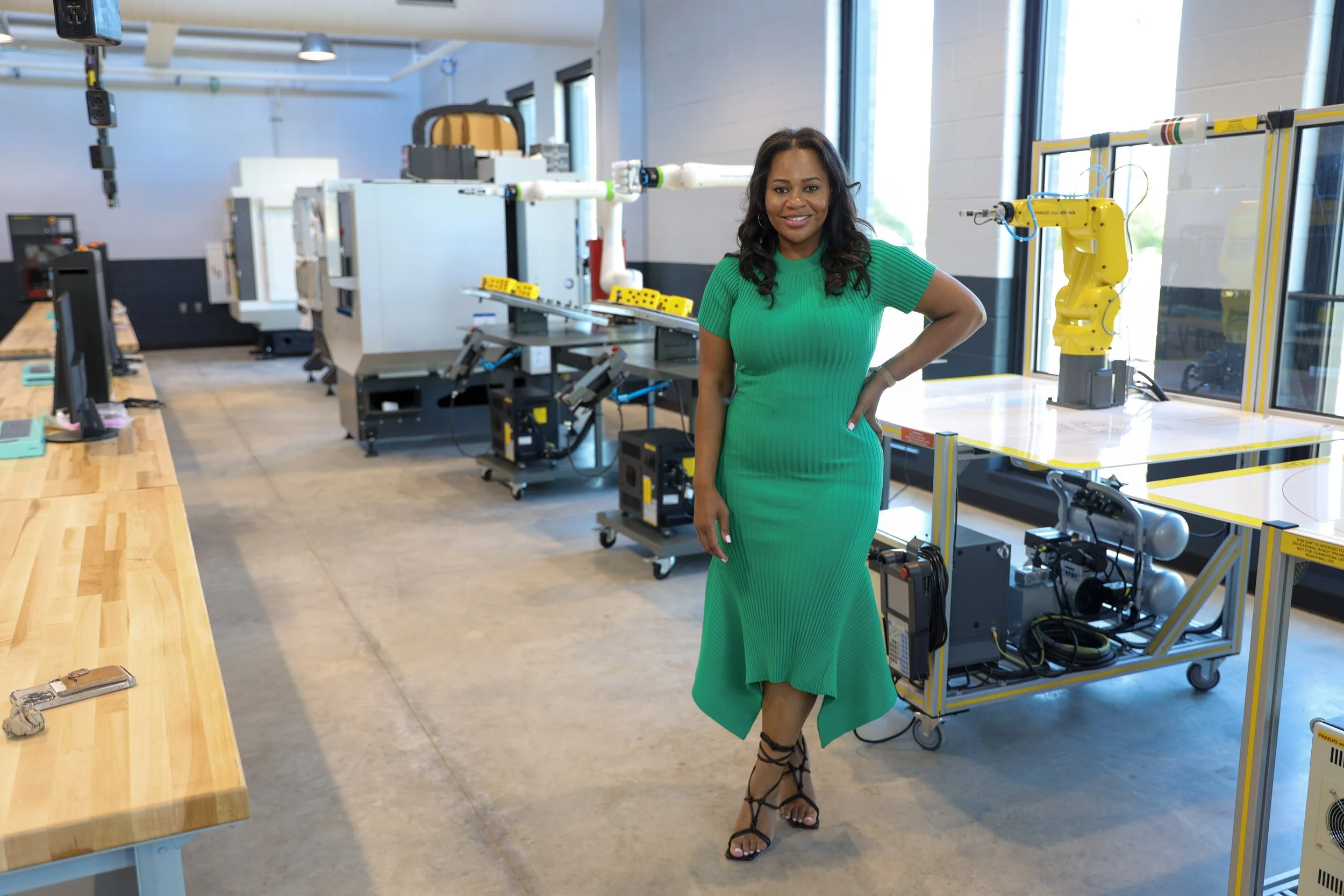 Woman in green dress standing in a modern industrial or technology lab with robotic equipment and workstations.