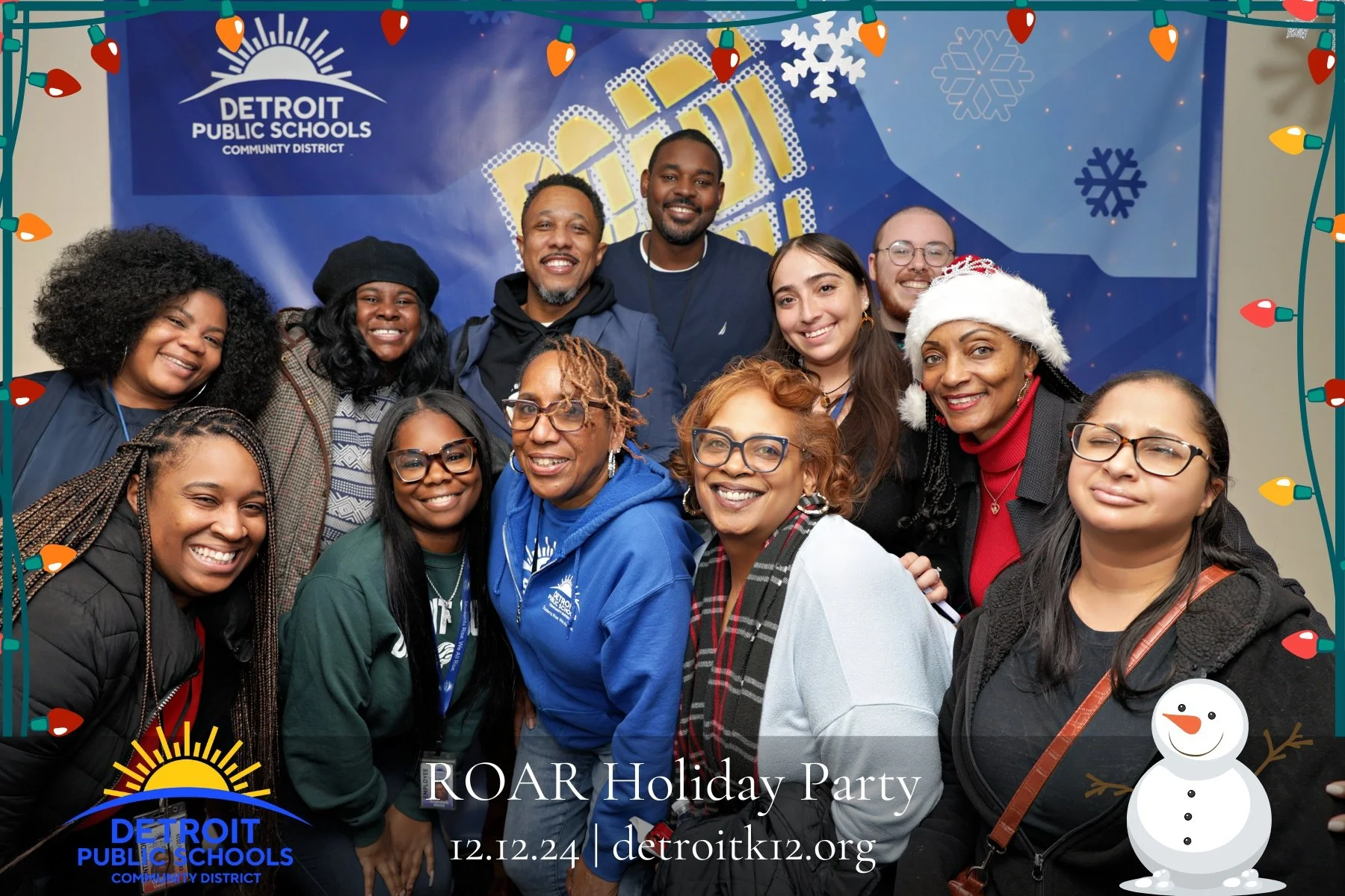 Group of diverse people smiling at Detroit Public Schools ROAR Holiday Party, December 12, 2024, with holiday decorations and a snowman graphic in the border.