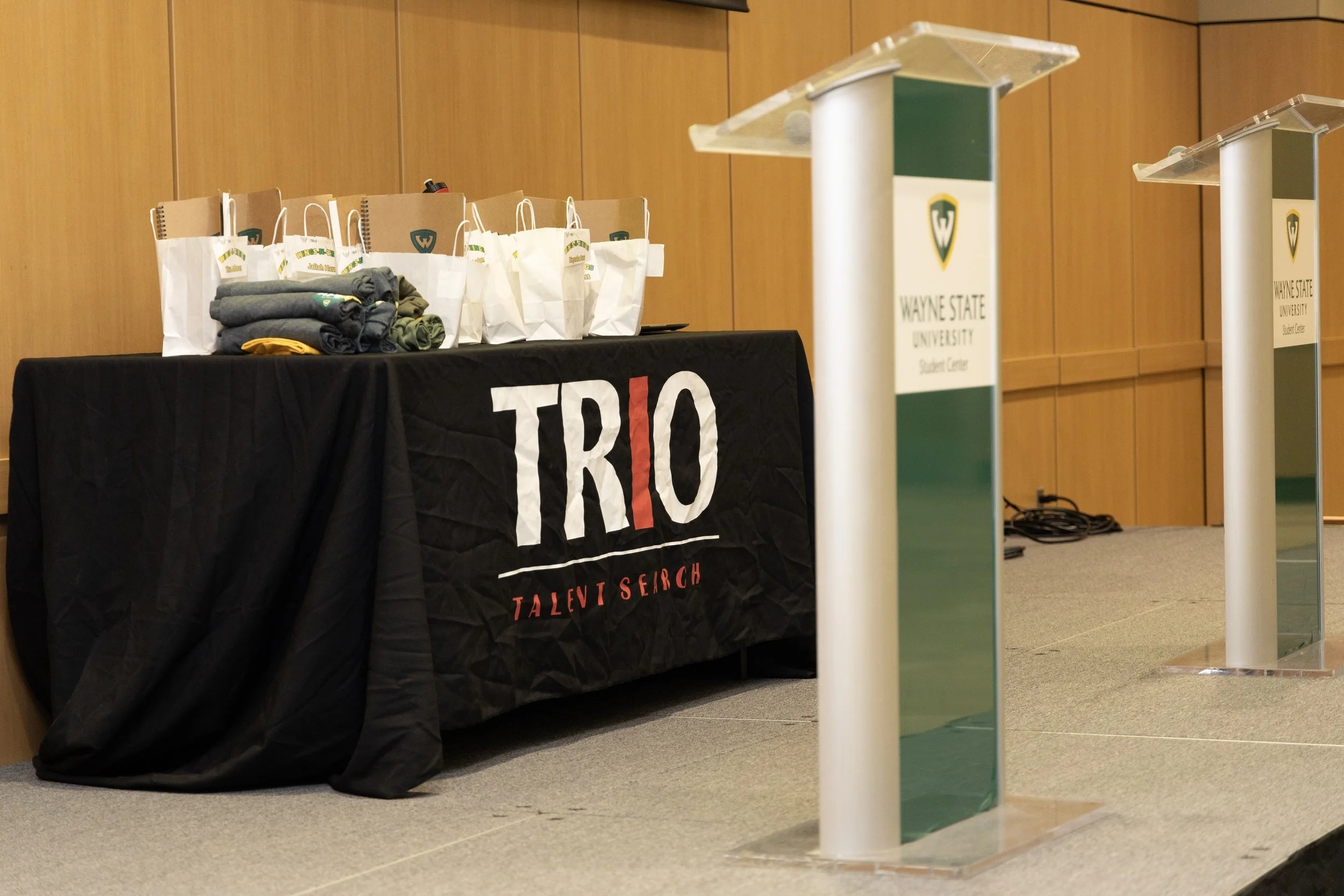 Table with Wayne State University branding, gift bags, and folded clothing items in a conference room.