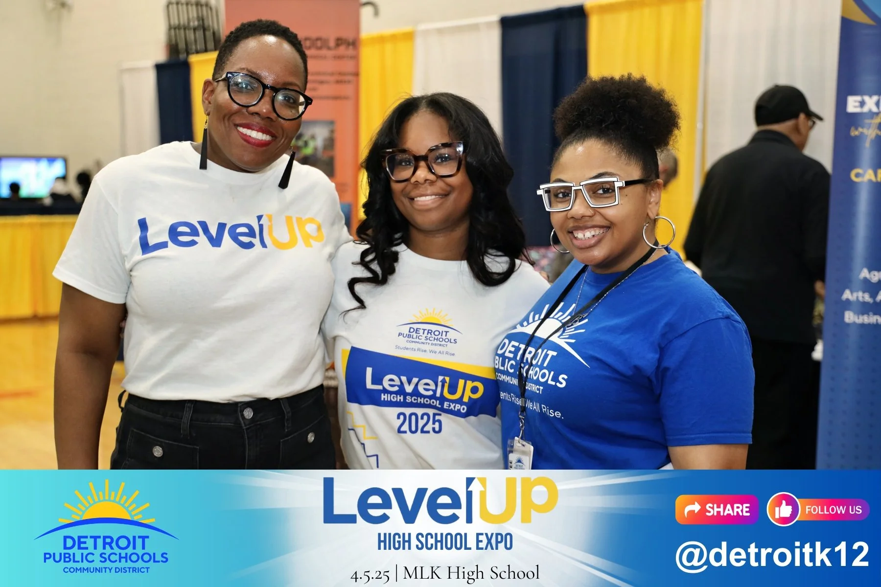 Three women smiling at the Detroit Public Schools Level Up High School Expo, wearing Detroit Public Schools T-shirts and standing in front of a colorful background at the event.