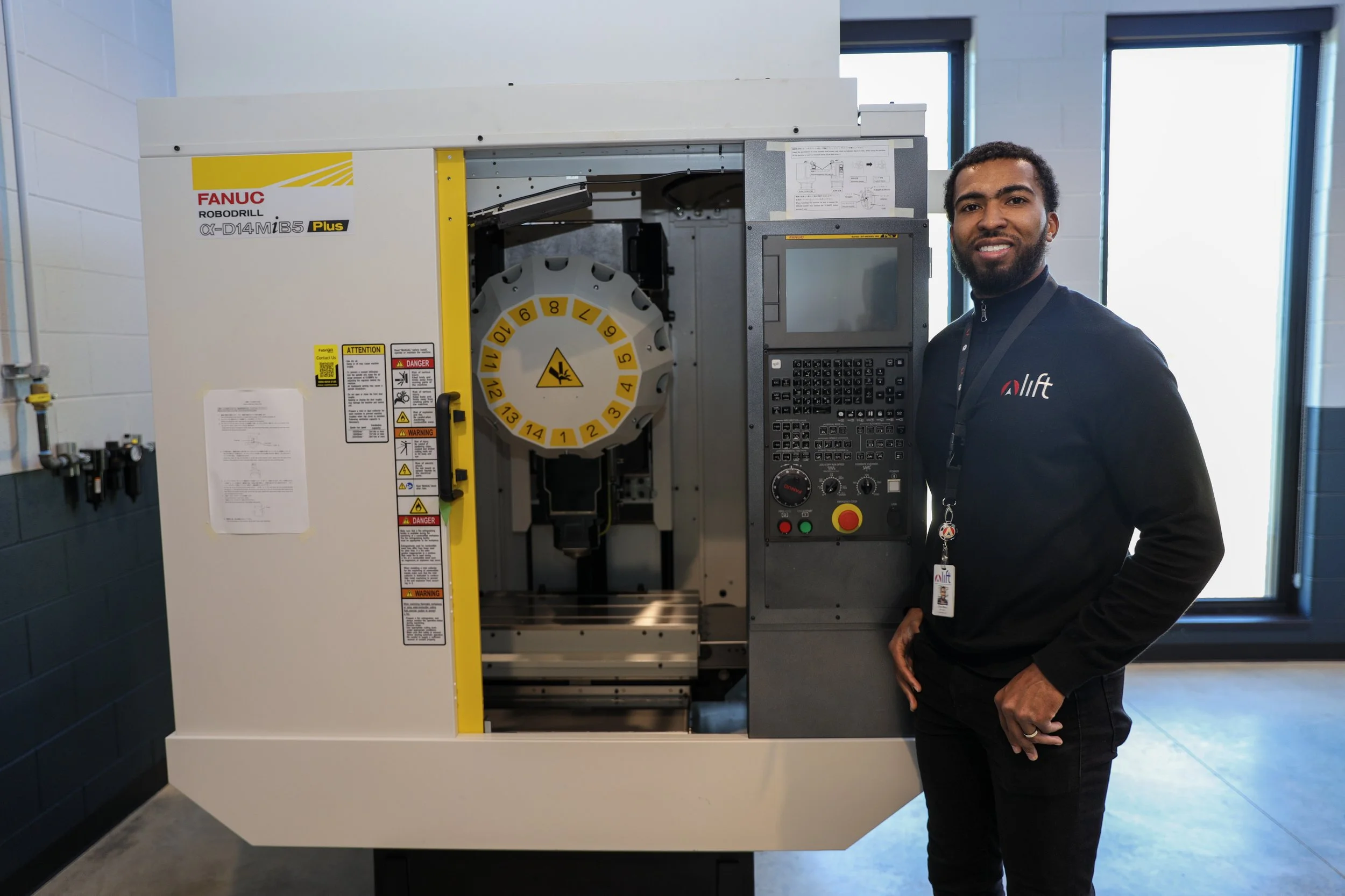 A man standing next to a FANUC robotic milling machine in an industrial setting, with his right hand resting on his hip and smiling at the camera.