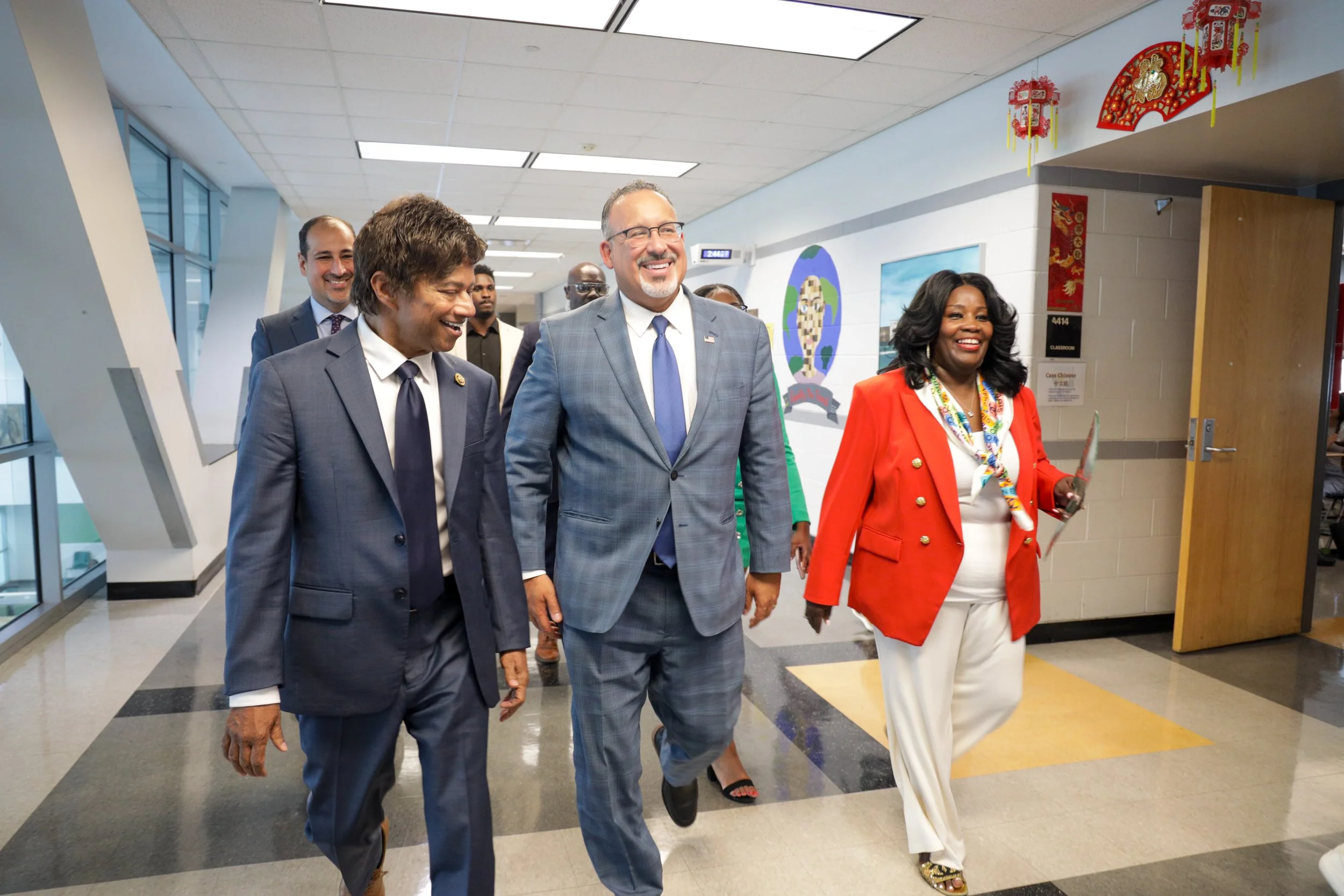 A group of six diverse adults walking in a hallway, smiling and engaging with each other, with decorations on the wall and a door in the background.